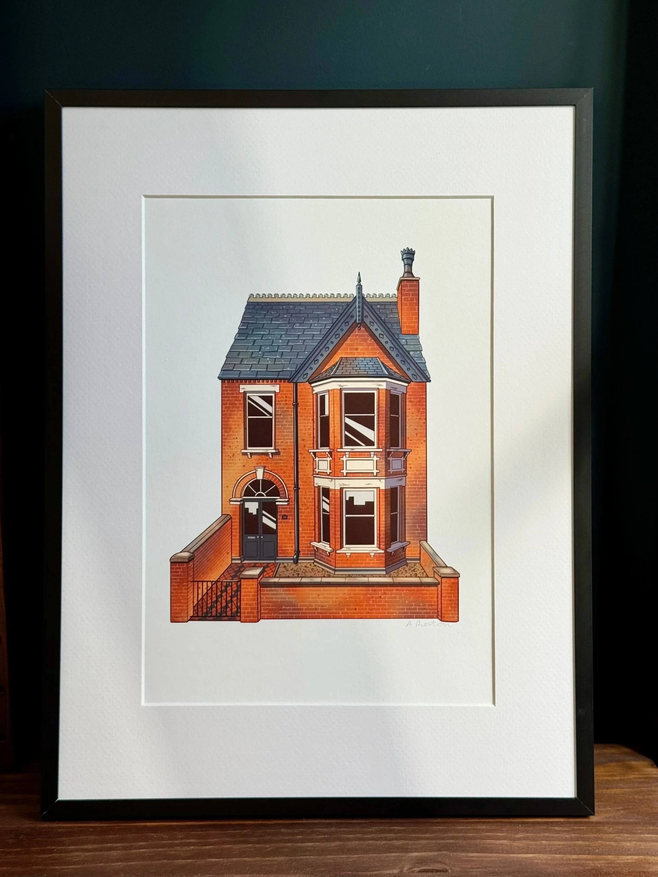 A framed illustration of a red brick Victorian-style house with a gabled roof, bay windows, and a brick fence in front.