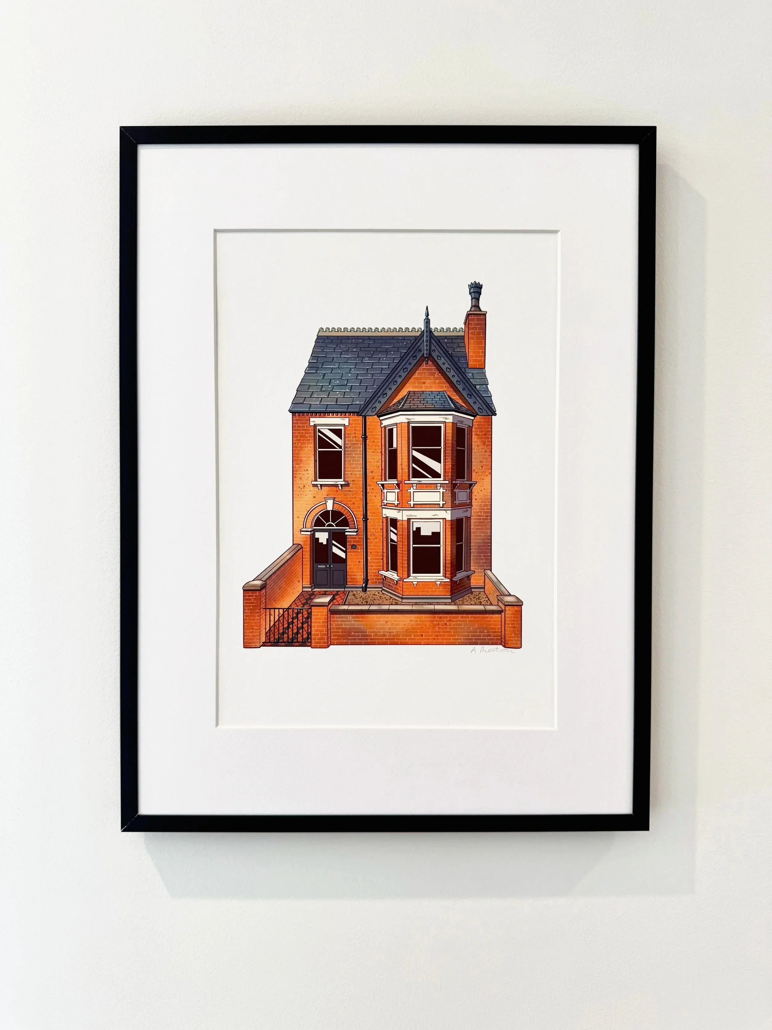 A framed architectural drawing of a red brick Victorian house with a dark grey roof, large front windows, a small front yard, and a black front door.