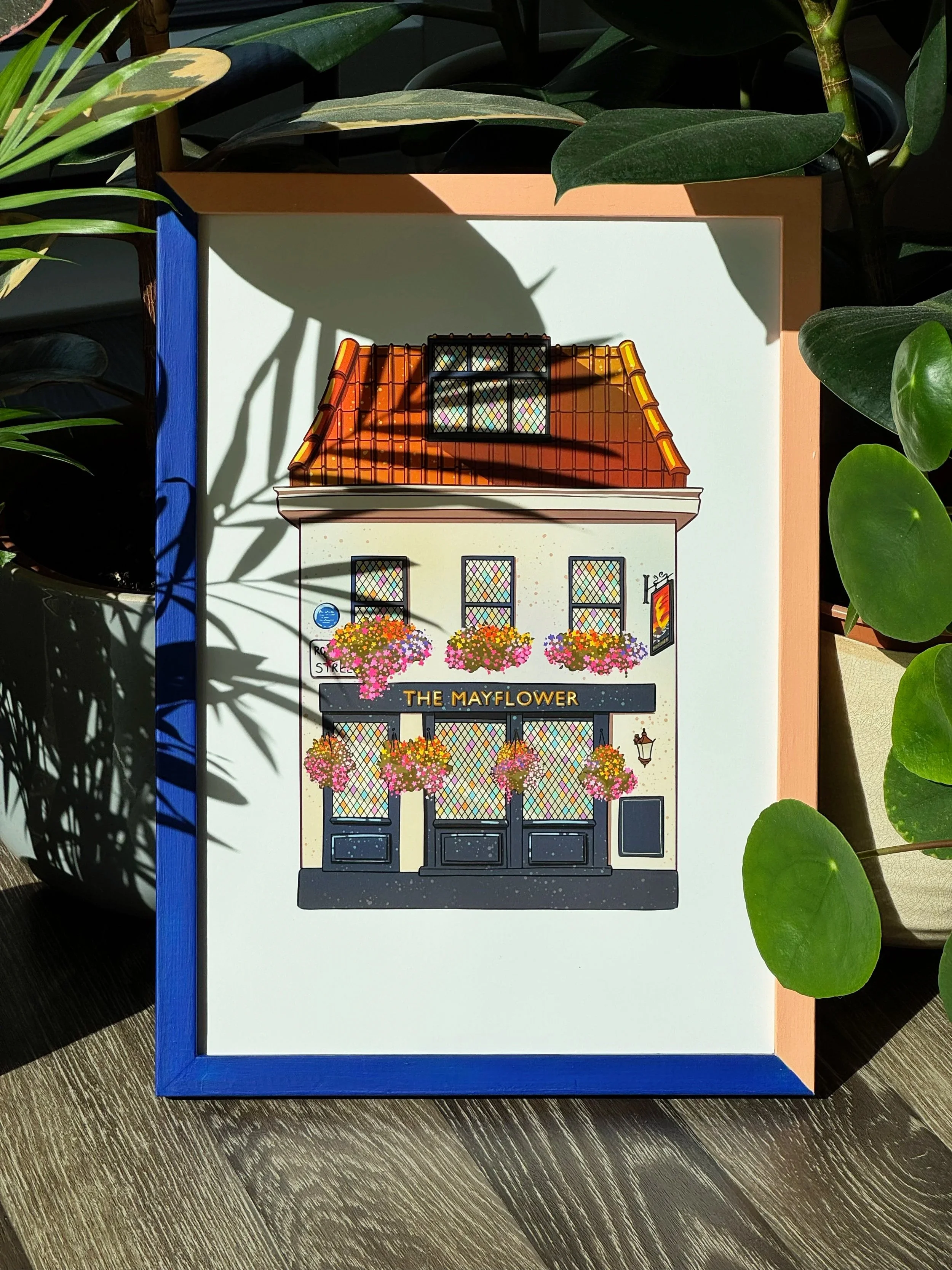 Illustration of a building facade with a sign that reads 'The Mayflower,' featuring flower baskets and windows with colorful windowpanes, surrounded by green plants and shadows.