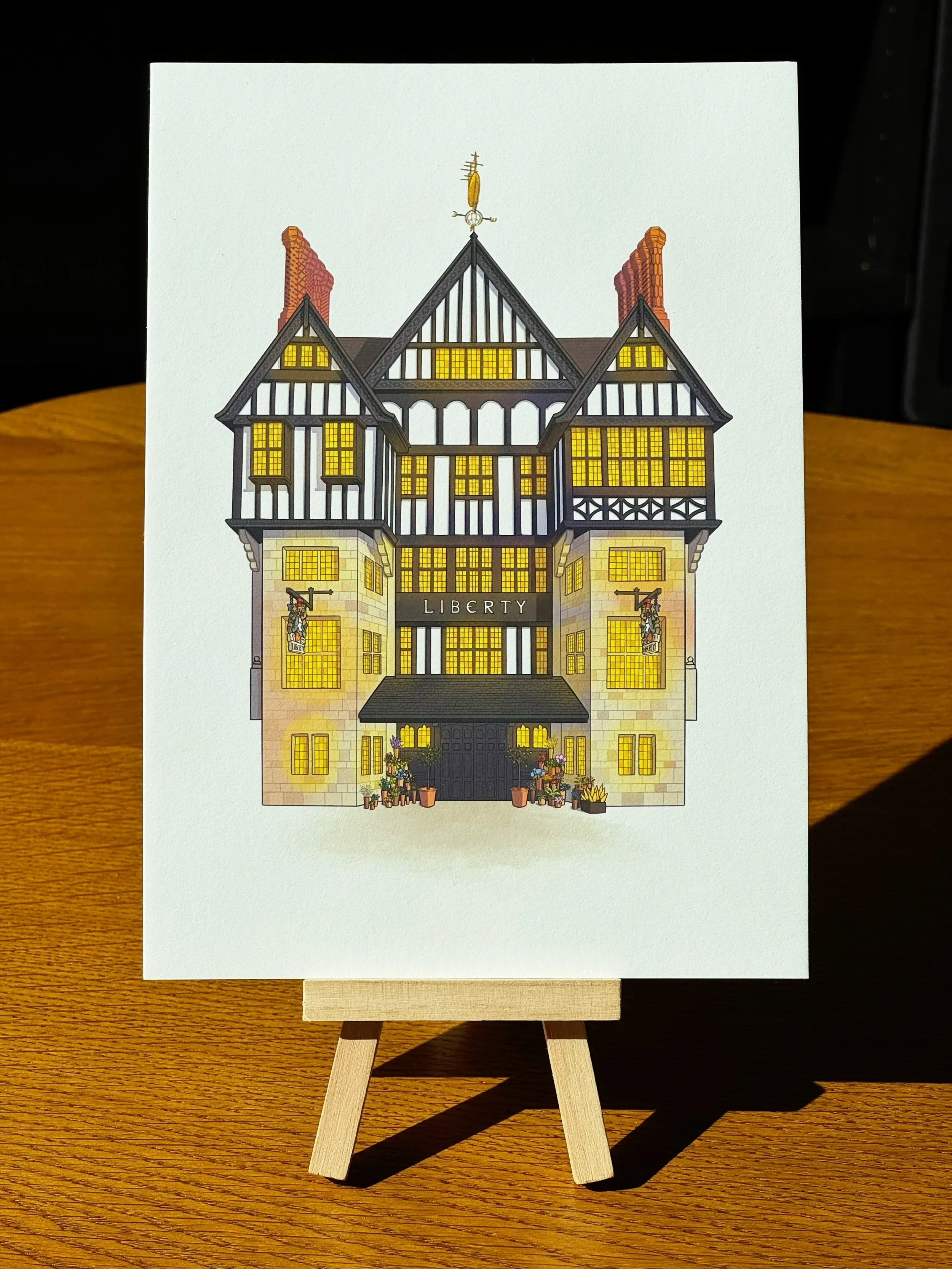A detailed illustration of a historic building labeled 'Liberty' with illuminated windows and decorative elements, displayed on a small wooden easel on a wooden table.