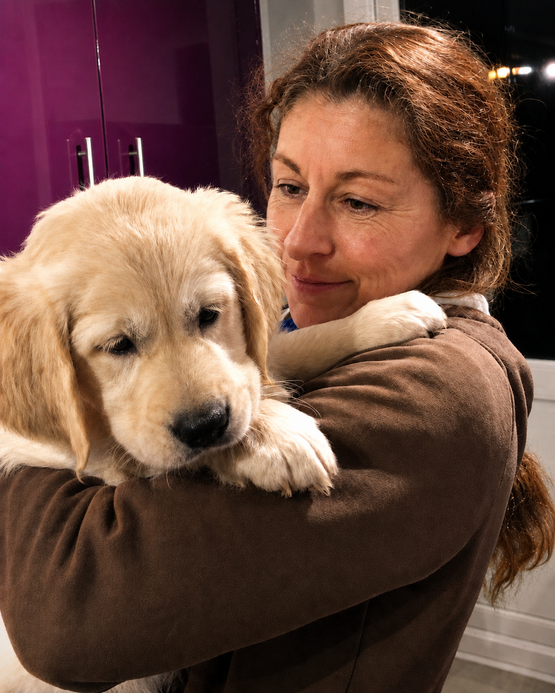 A woman holding a young golden retriever puppy in her arms indoors.