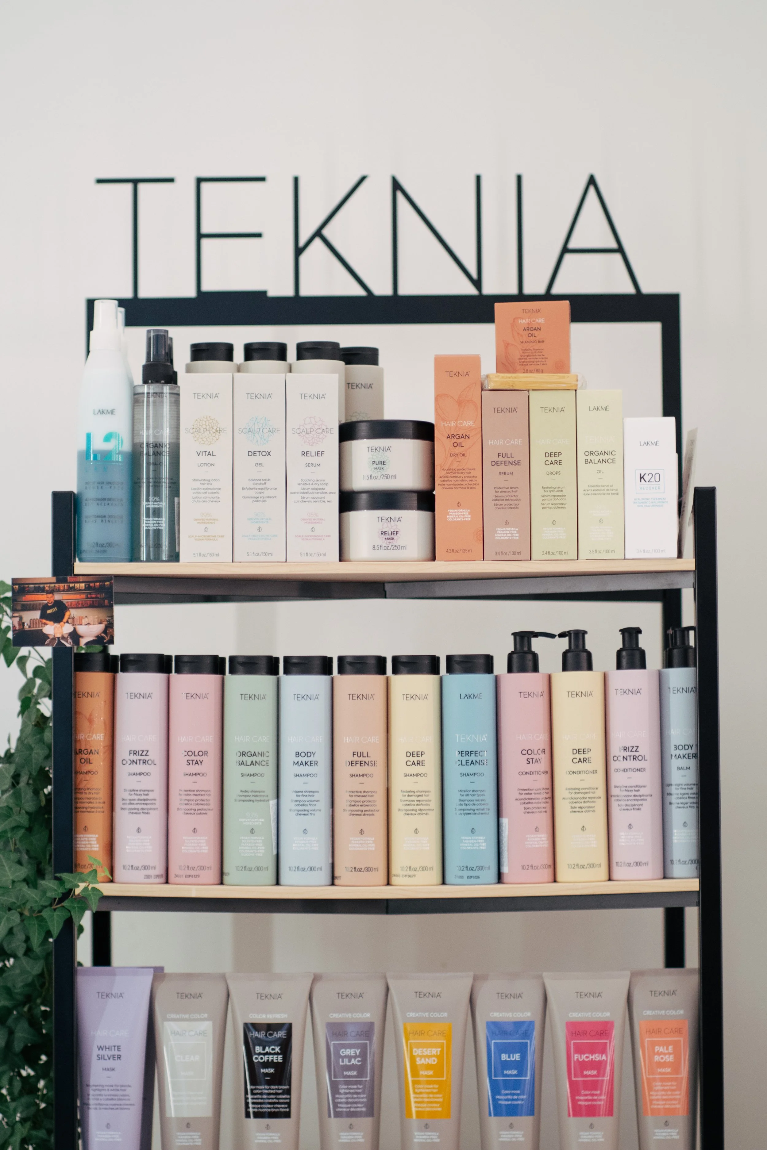 Display of various hair care products on a shelf with a large sign that says 'TEKNIA' in the background.