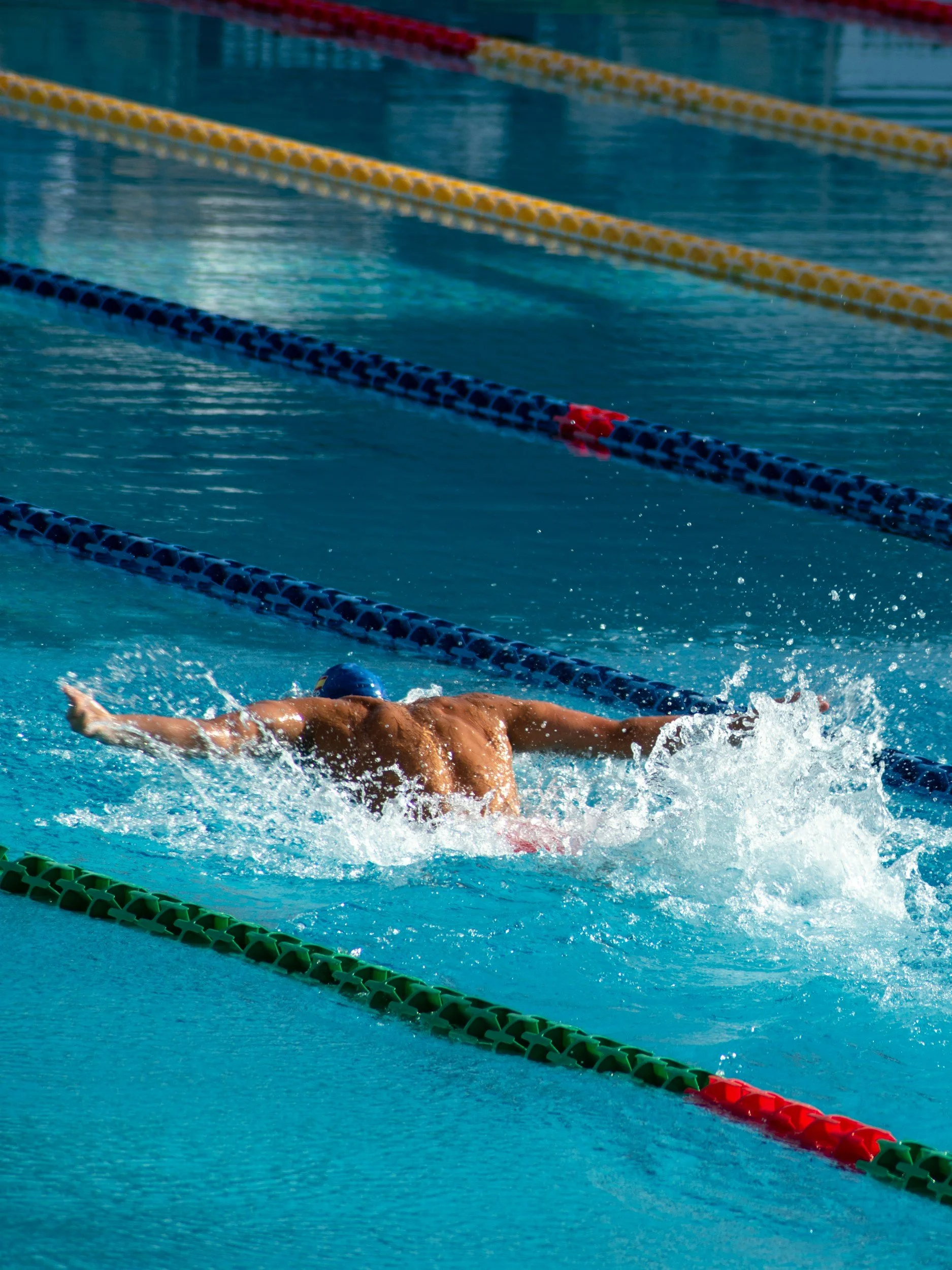 Swimmer doing the butterfly stroke in an outdoor swimming pool with multiple lane dividers.