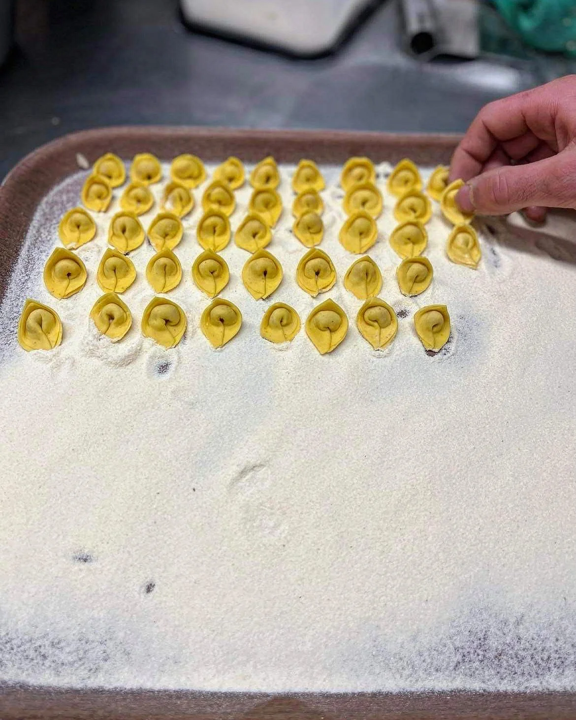 Vue d'une plaque de farine avec des pâtes fraîches faites à la main, ressemblant à des tortellinis, avec une main qui place une pâte.
