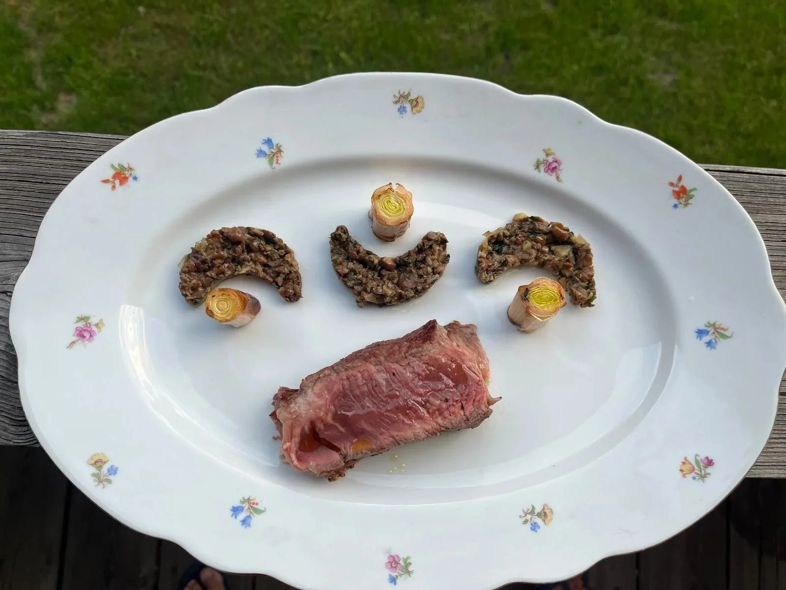 Une assiette avec côte de bœuf, petits champignons et poireaux poêlés au barbecue. 