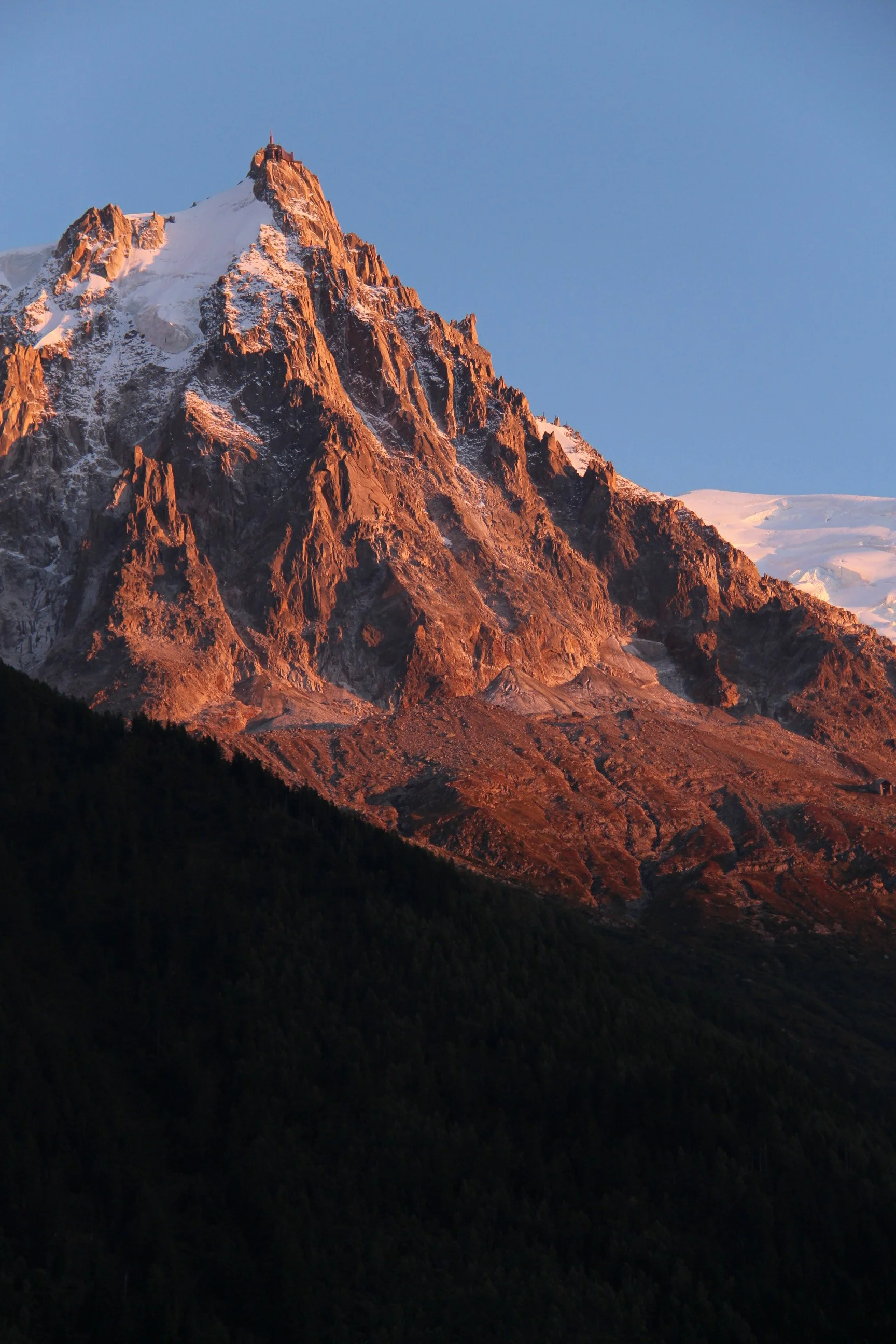 Une montagne enneigée au coucher du soleil avec un sommet pointu, attire l'attention avec ses couleurs chaudes et ses rochers escarpés.