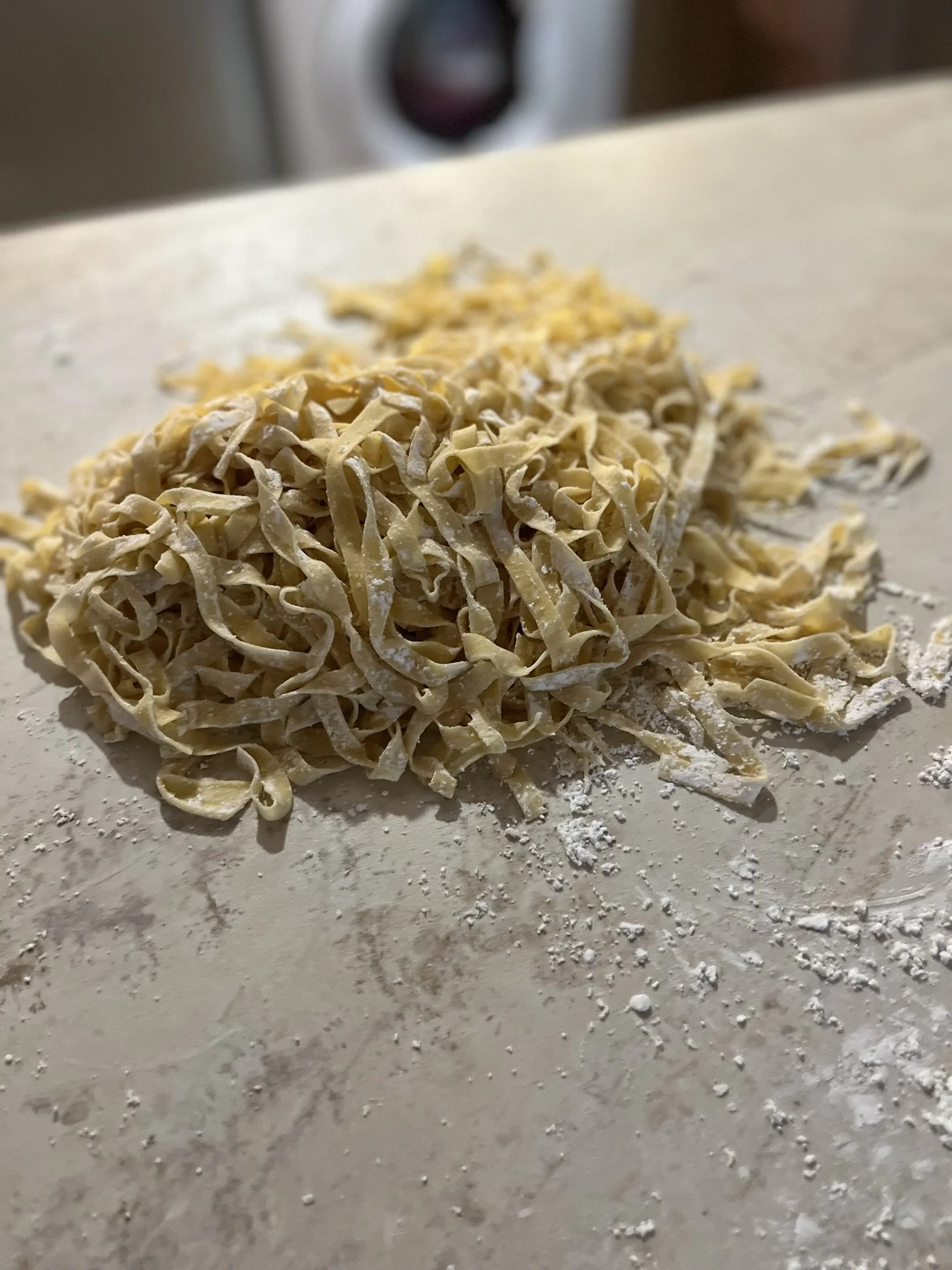 De la farine, des pâtes faites maison en forme de tagliatelles, sur un plan de travail.