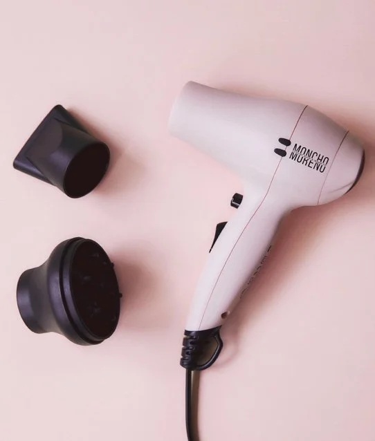 A white Conair dryer with black accents and two black attachments on a pink background.
