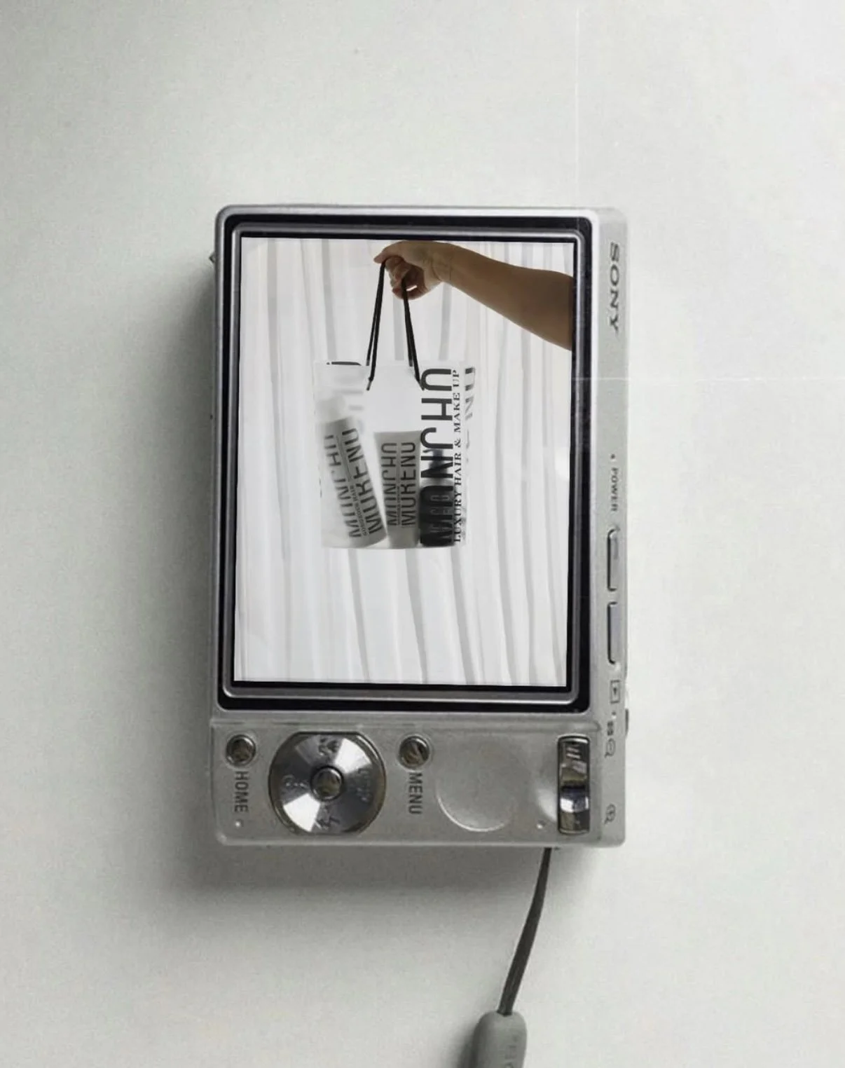 A Sony digital camera attached to a flat surface showing a reflection of a hand holding a shopping bag with the word 'MUNCH' on it.