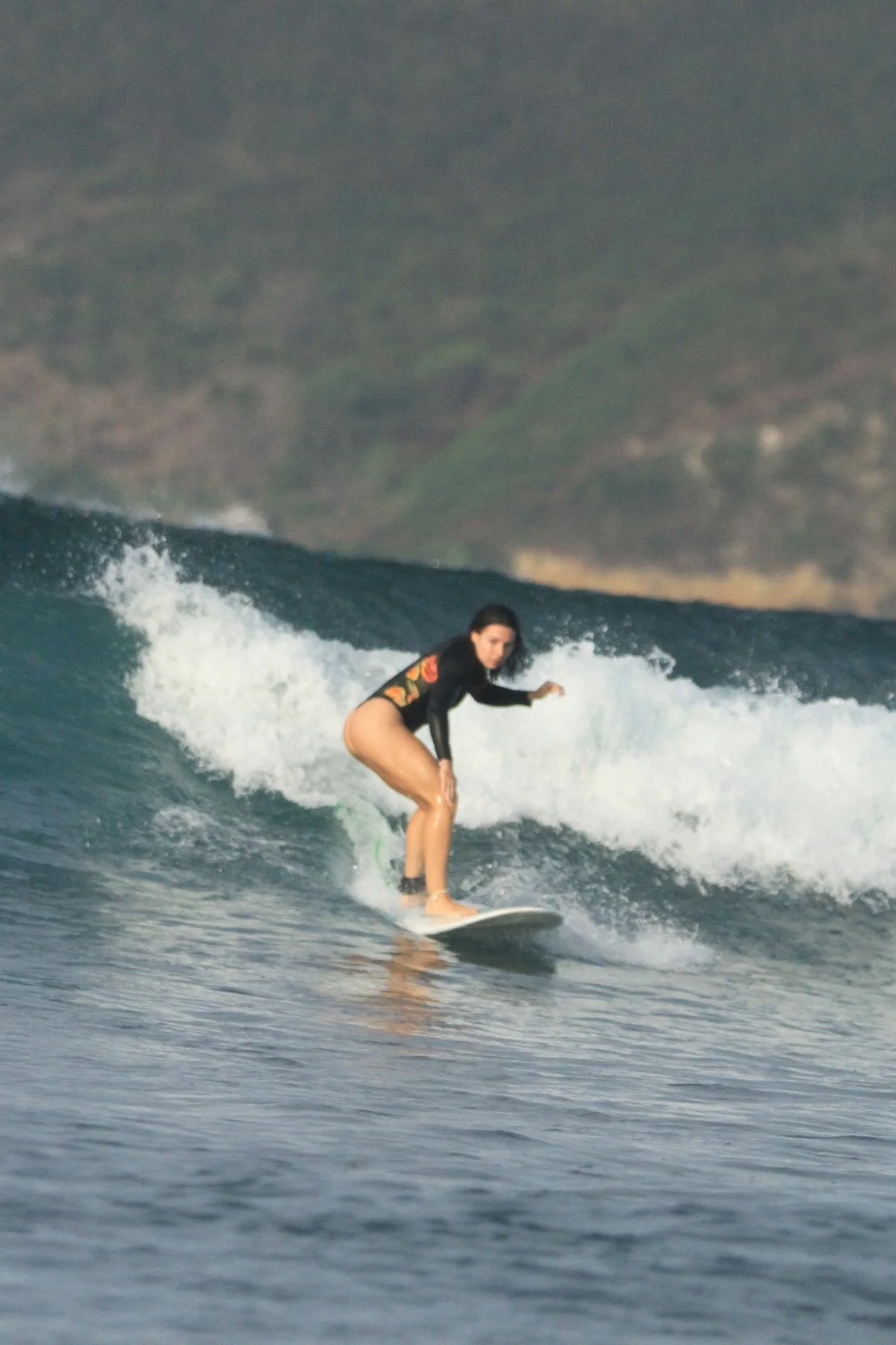 A woman surfing on a wave in the ocean with a blurry landmass in the background.