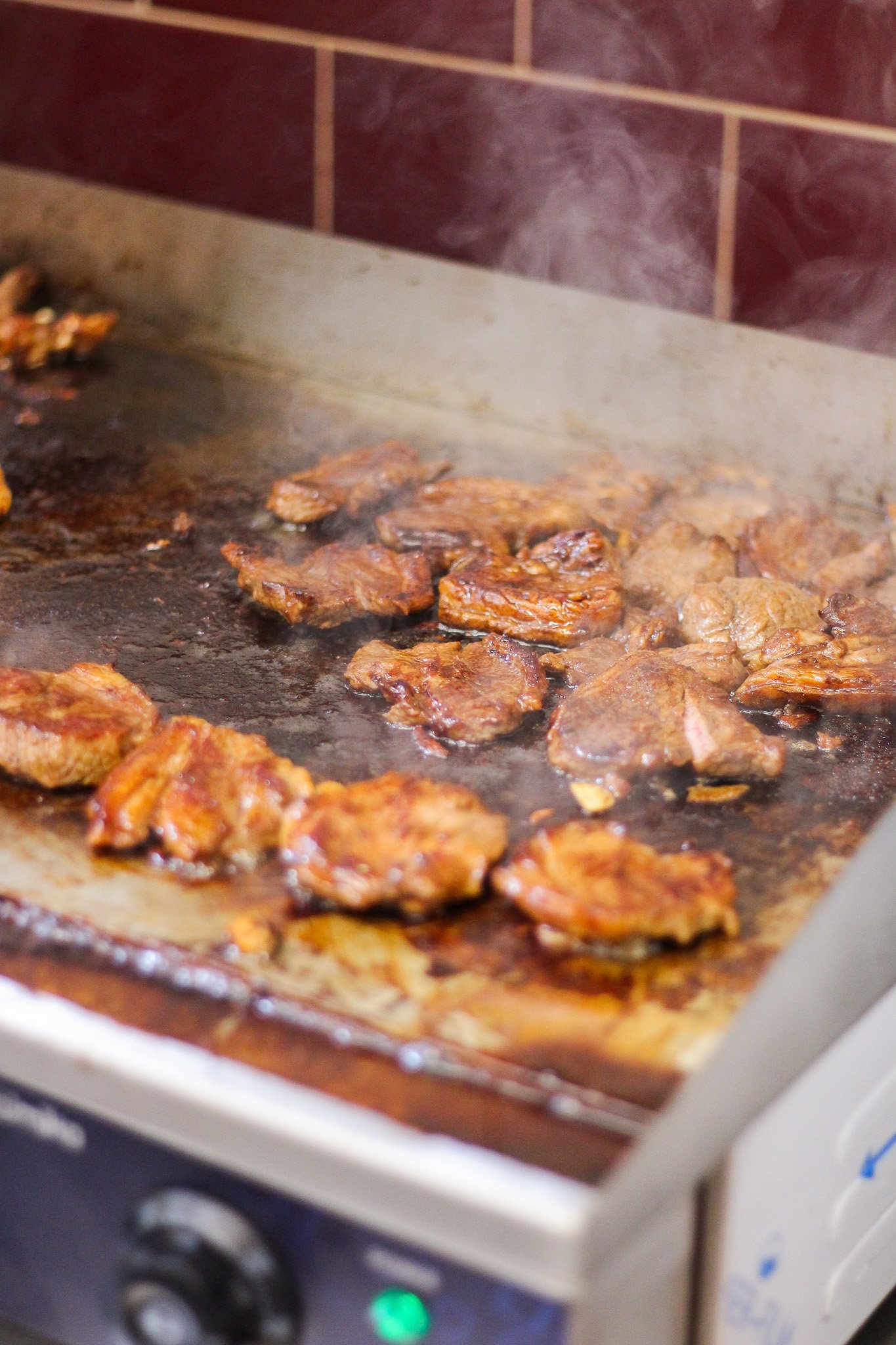 Meat being cooked on a griddle with sizzling and steam rising from it.