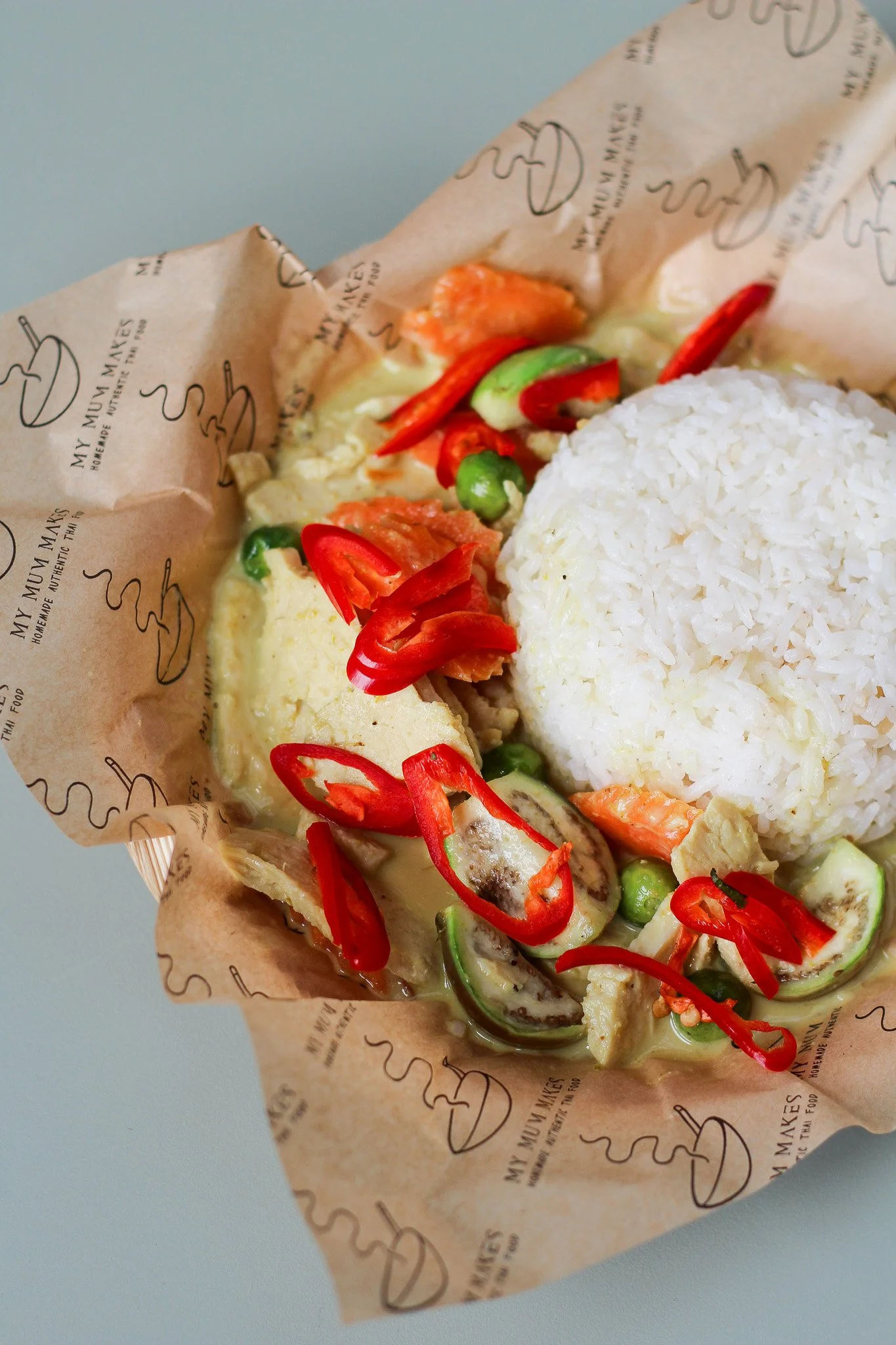 Vietnamese spring roll with white rice, red chili slices, cucumber, salmon, and creamy dipping sauce, served on decorative paper with the restaurant's logo.