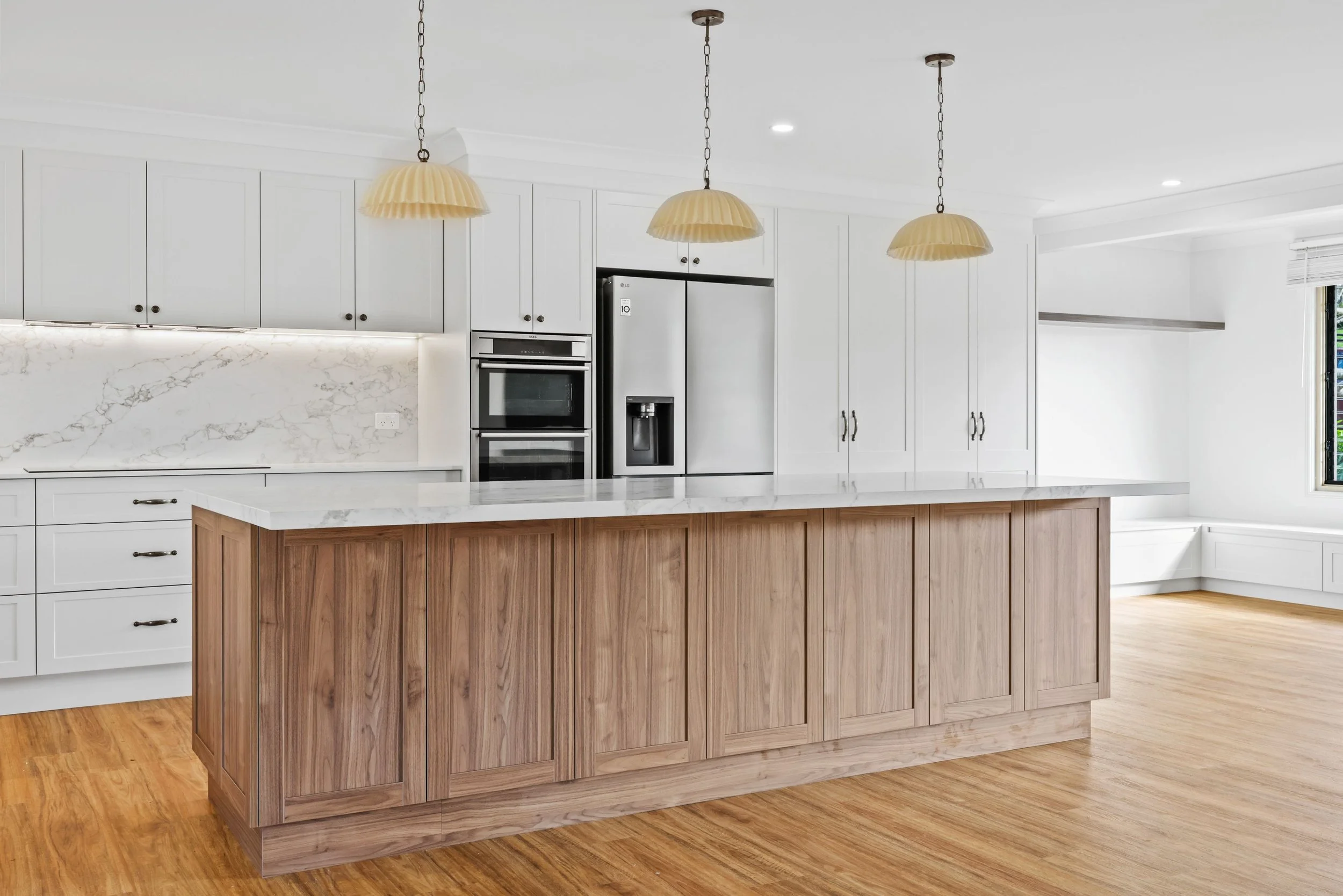 A modern kitchen with white cabinetry, a marble backsplash, and a wooden island. Three pendant lights hang from the ceiling, and the kitchen features stainless steel appliances.