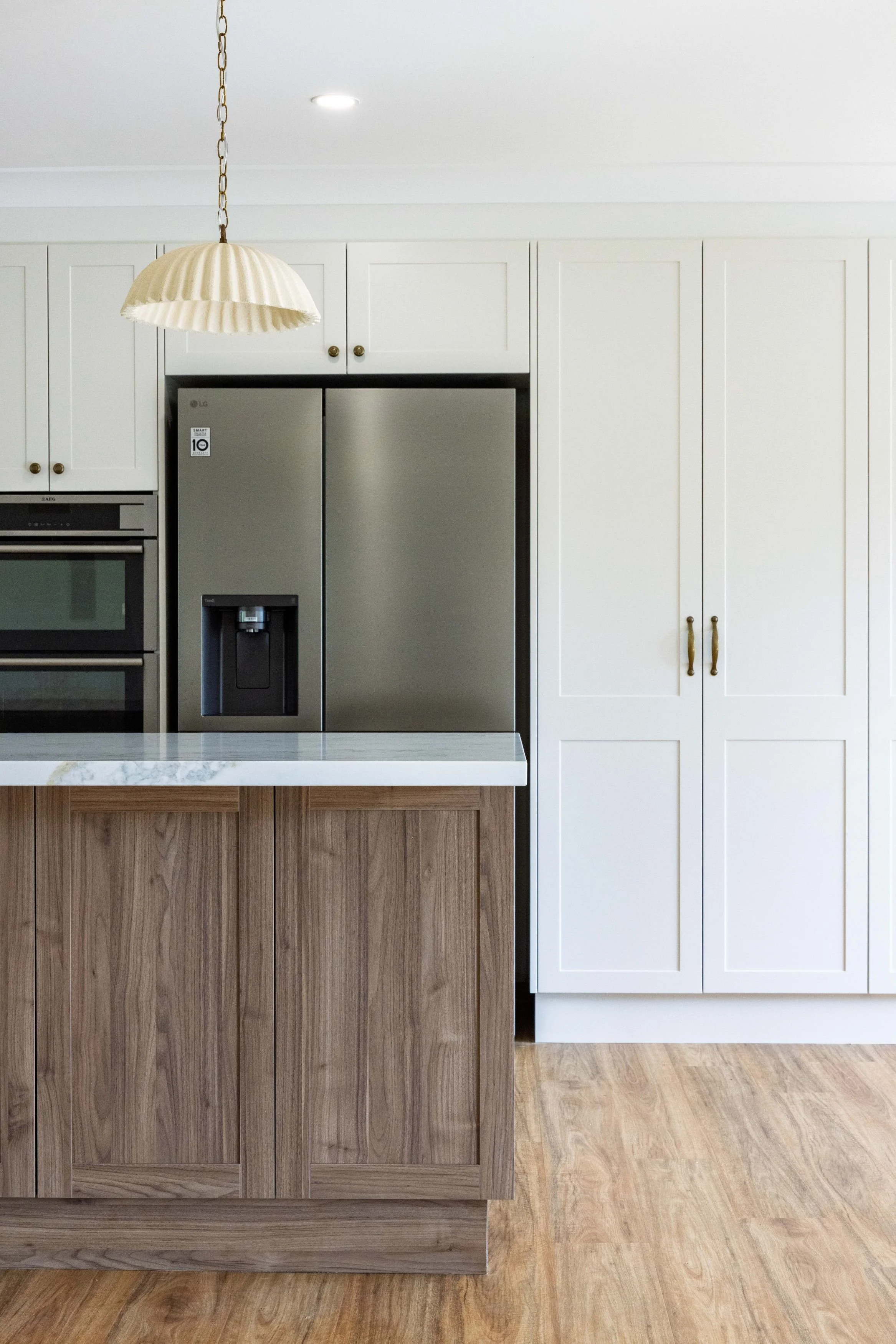 A modern kitchen with a white upper cabinet, stainless steel refrigerator, and a wooden kitchen island with a marble top. There's a beige pendant light hanging from the ceiling.