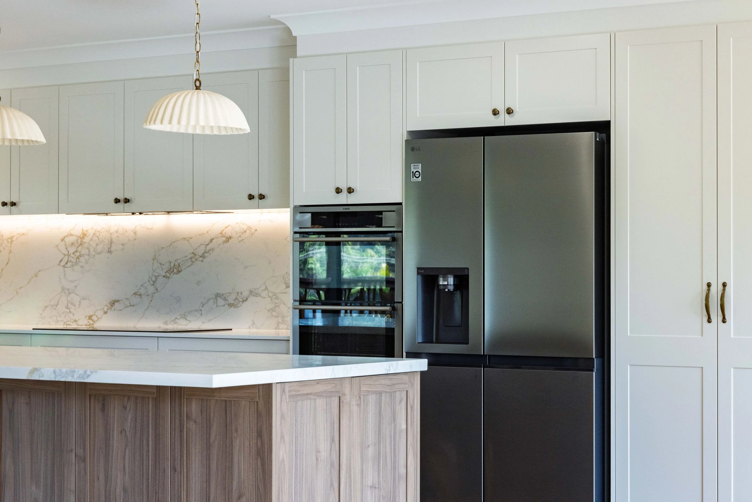 Modern white kitchen with marble backsplash and stainless steel refrigerator.