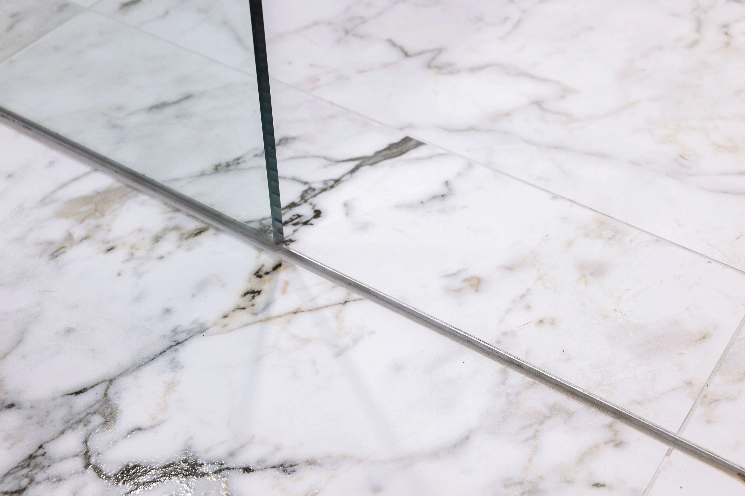 A close-up of a corner of a marble floor with a mirror and a metal strip running along the edge.