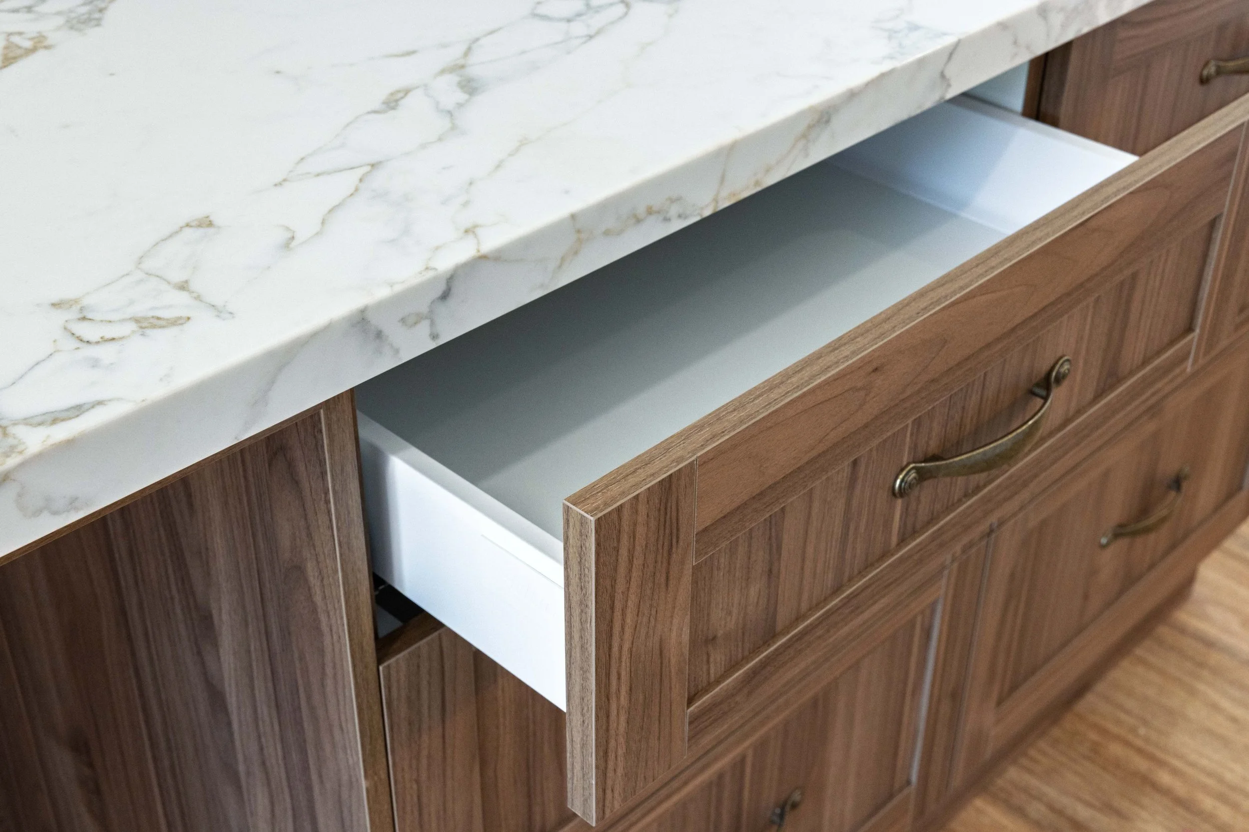 Open kitchen cabinet with a marble countertop and wooden drawers.