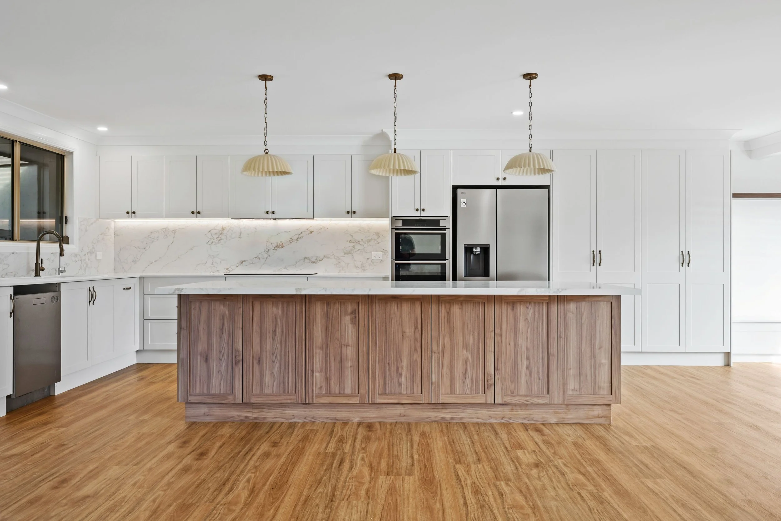 Modern kitchen with white cabinets, marble backsplash, wooden kitchen island, and three pendant lights hanging from the ceiling.