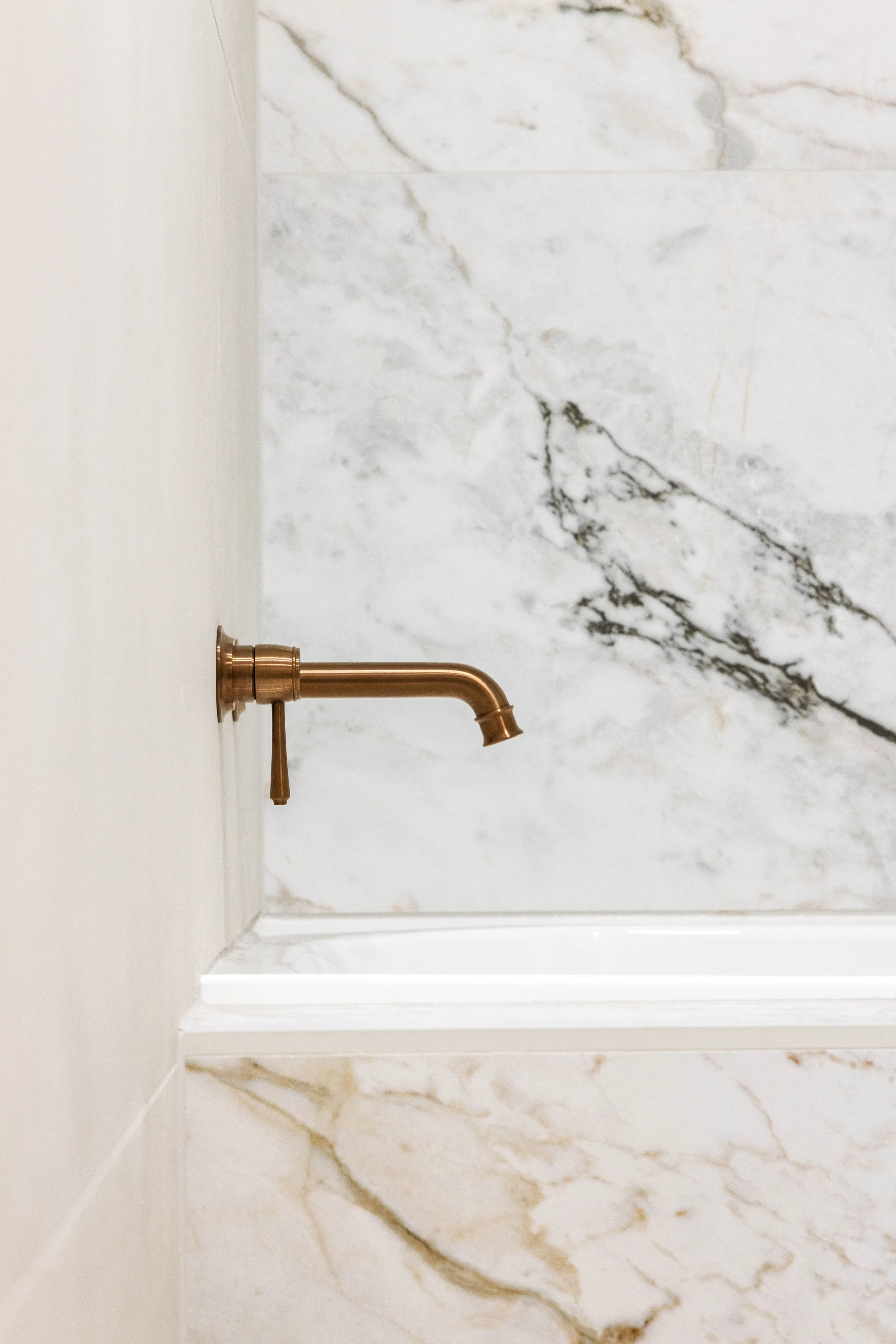 Close-up of a copper bathroom faucet with a marble wall background.