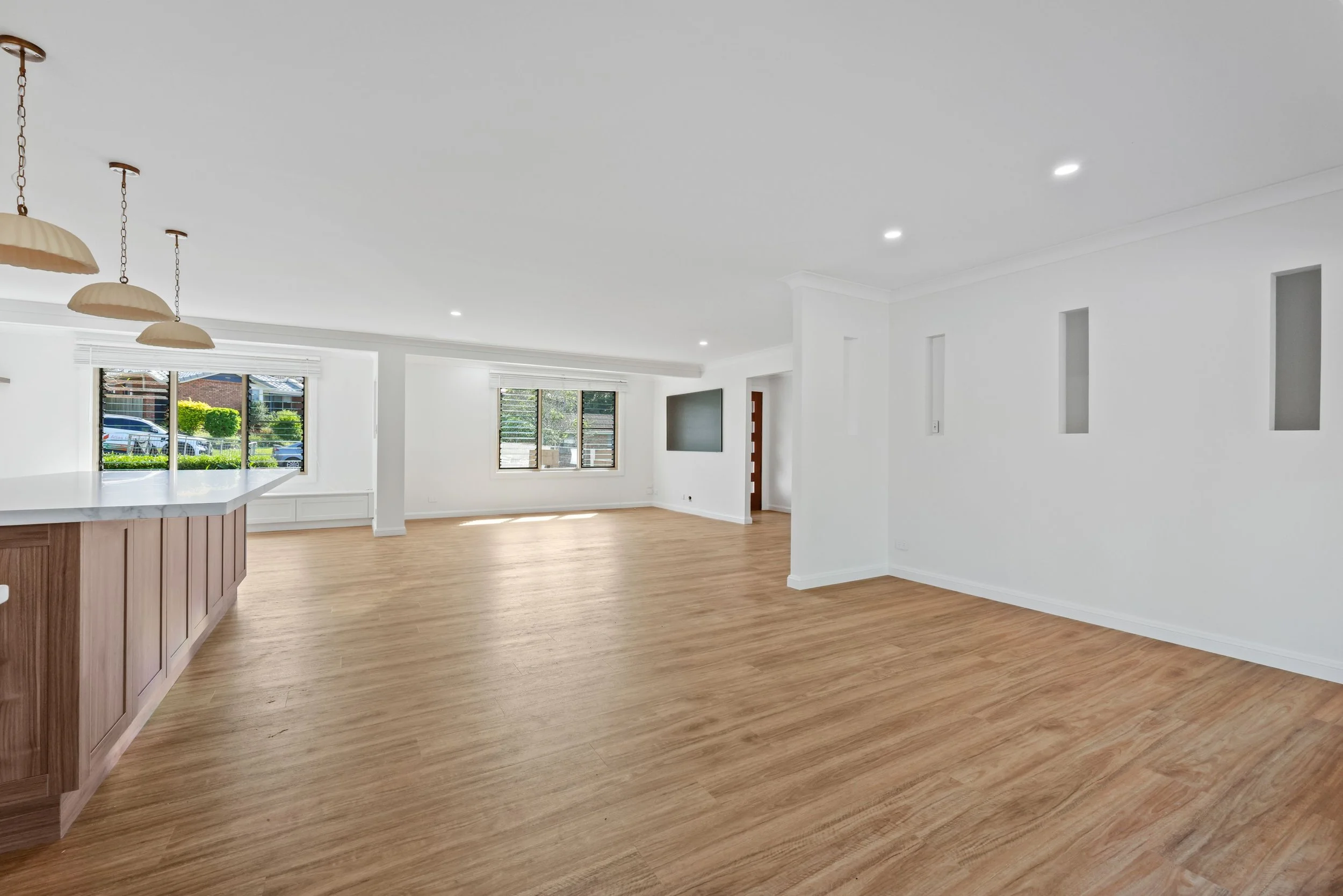 An open-plan living area with a kitchen island, large windows, hardwood flooring, and white walls with built-in niches.