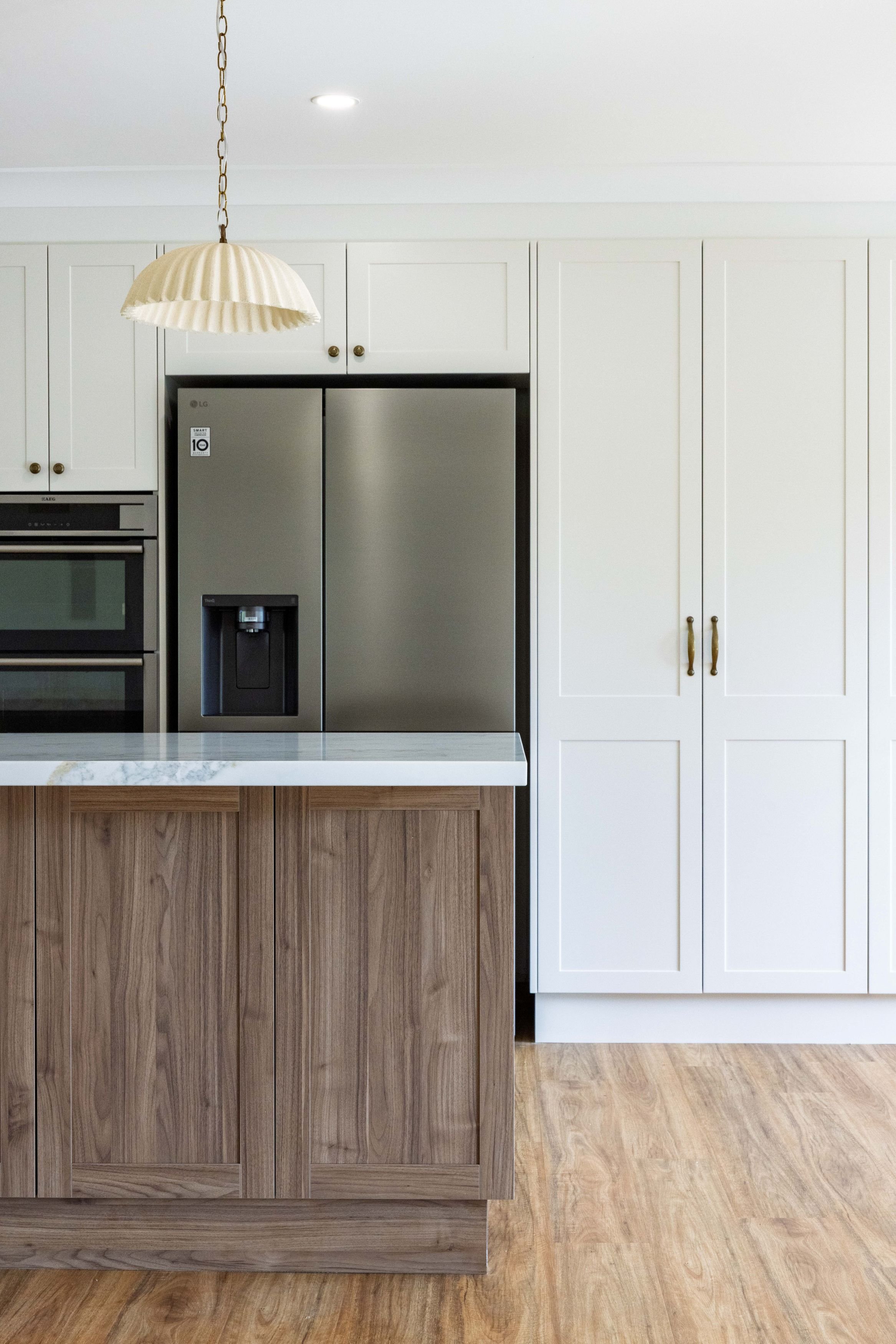 Kitchen with white cabinets, stainless steel side-by-side refrigerator, wooden island with a marble top, and wooden flooring.