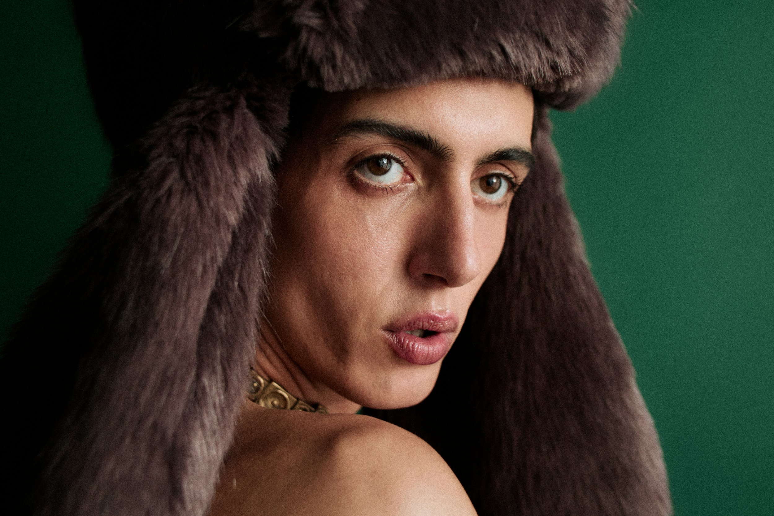 A woman wearing a brown fur hat and coat with a green background.