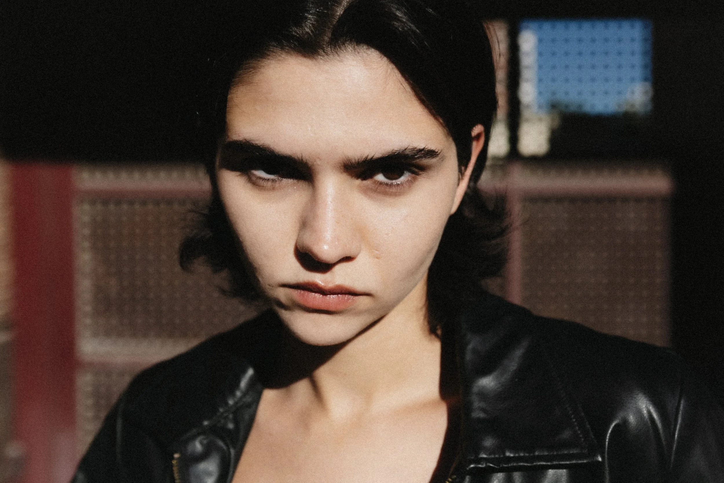 Close-up of a woman with dark hair, intense eyes, and a serious expression, wearing a black leather jacket.
