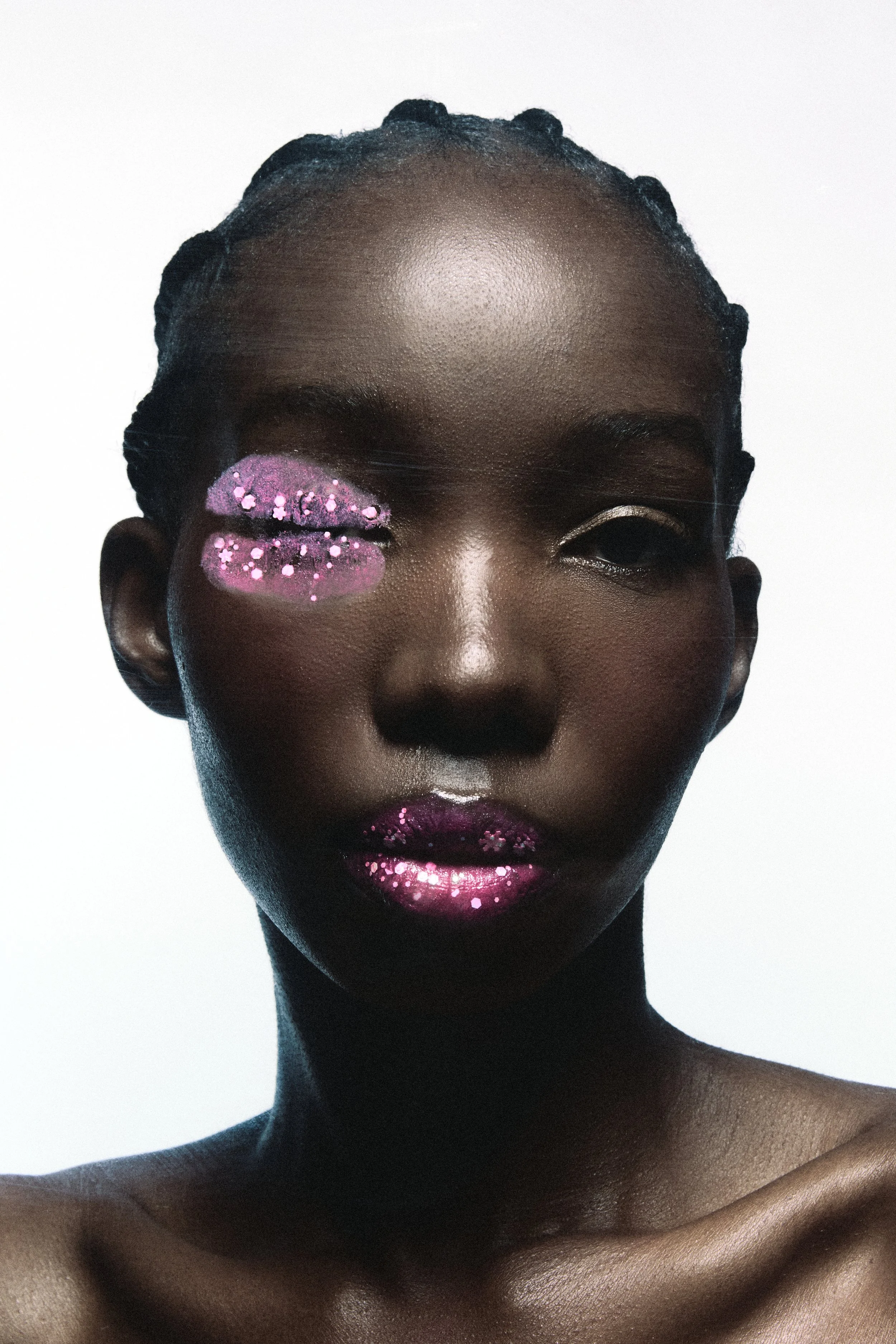 Close-up portrait of a Black woman with styled hair, with pink glittery face makeup on her cheeks and lips, against a plain light background.