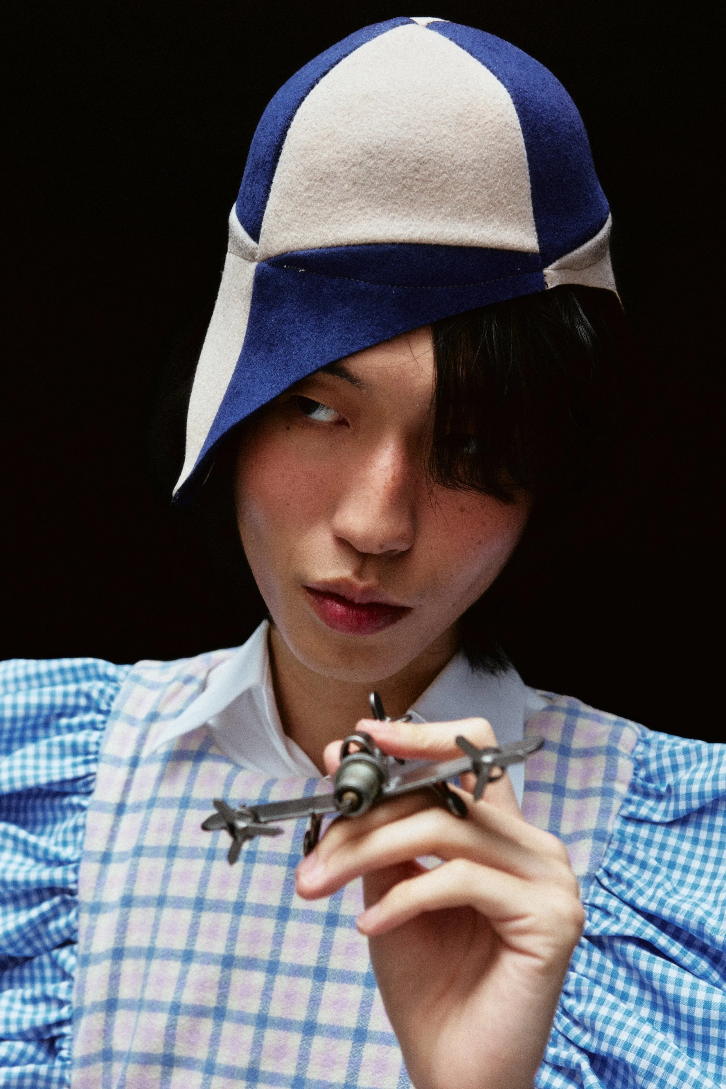 A person with dark hair, wearing a blue and white checkered shirt and a colorful cap, holding a torpedo-shaped object.