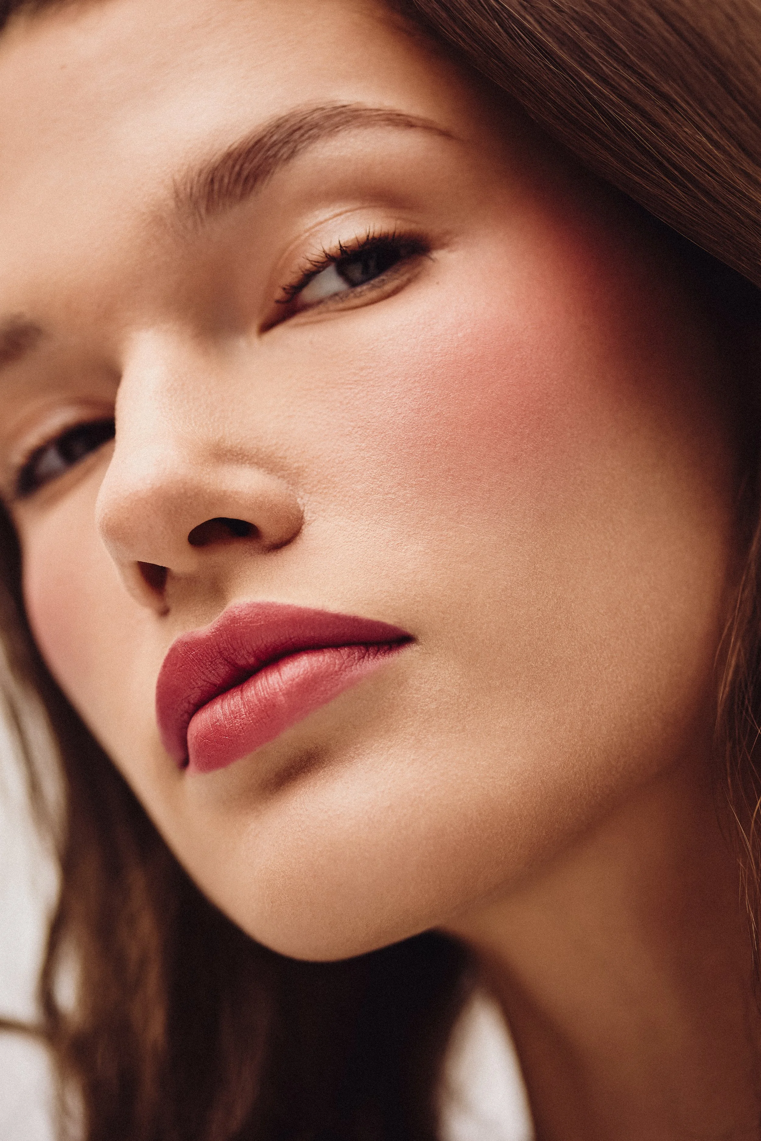 Close-up of a woman's face showing her eye, eyebrow, nose, and lips, with smooth skin and makeup, including lipstick.