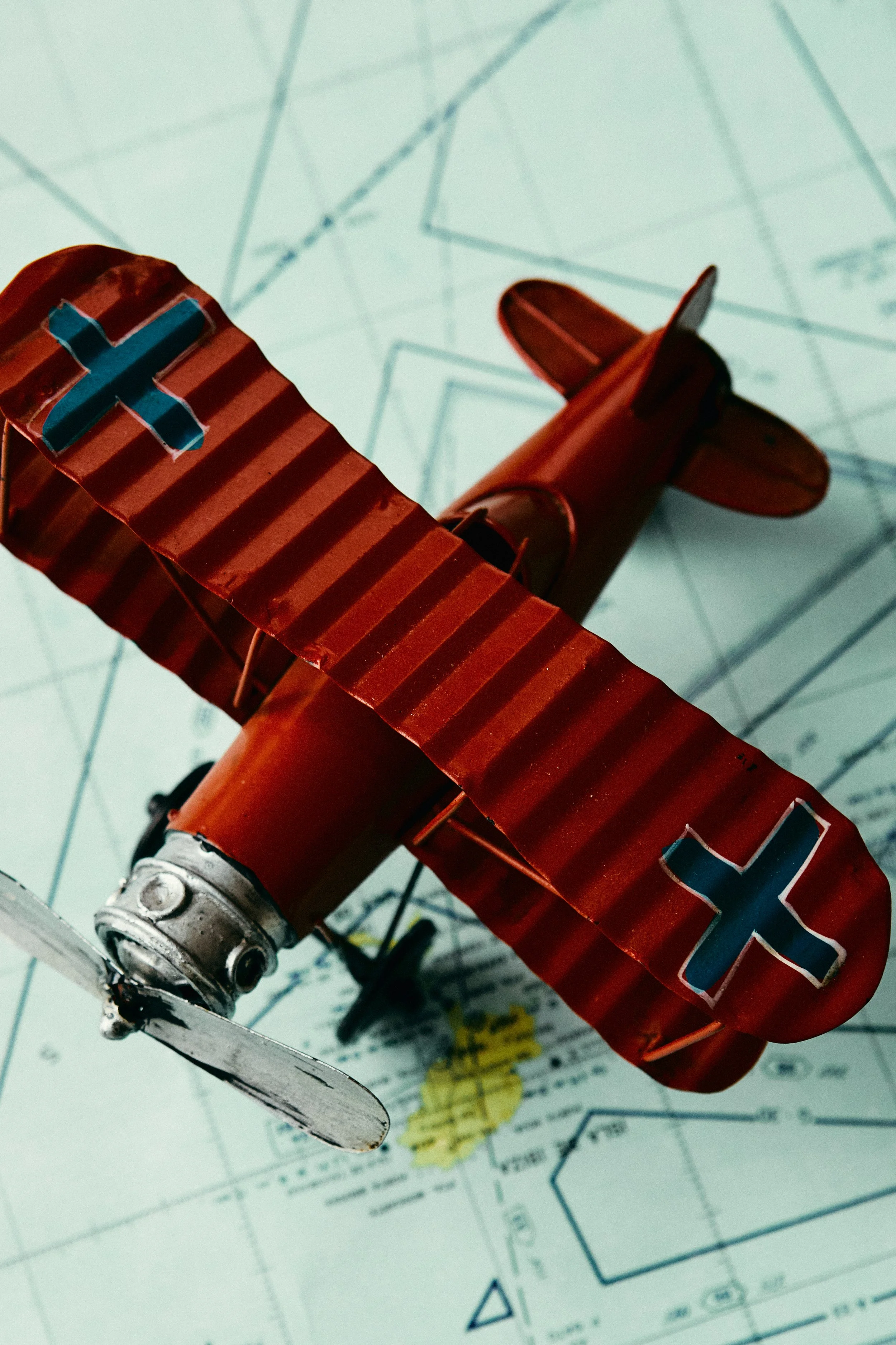 Close-up of a small, vintage orange and brown airplane model with a blue plus sign on the wing, resting on top of a detailed map or technical drawing.