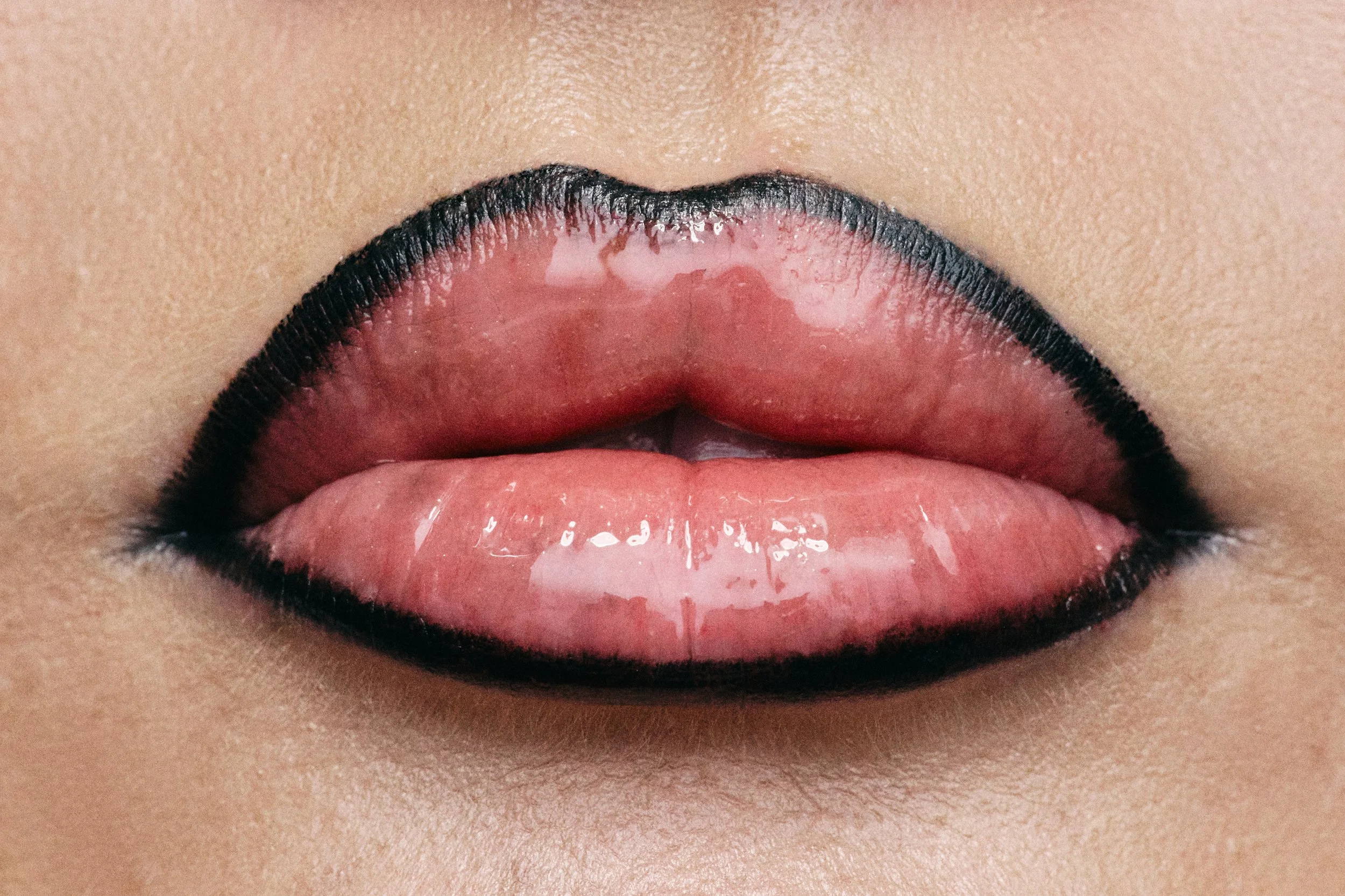 Close-up of lips with black lipstick and glossy finish, showing the surrounding skin.