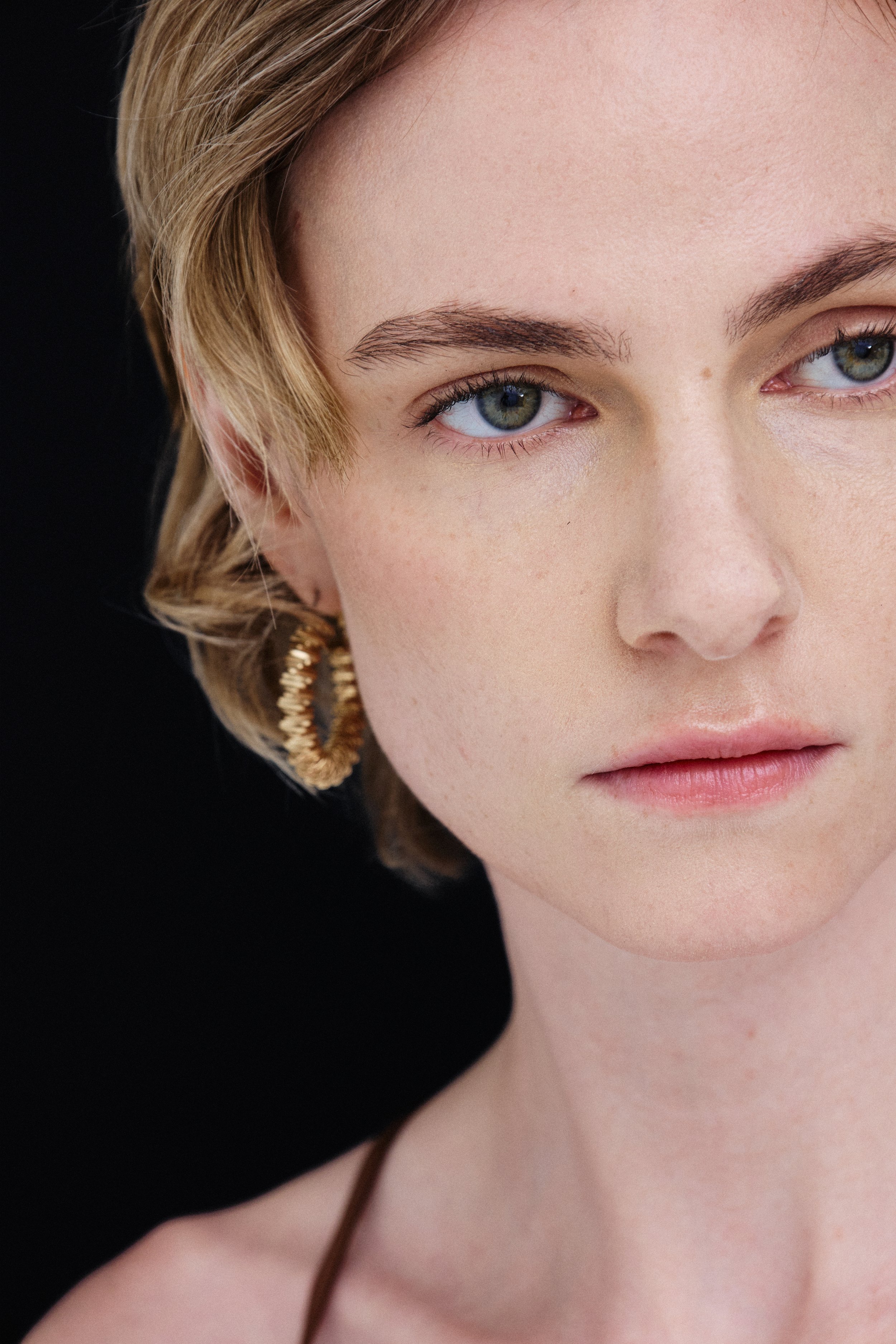 Close-up of a woman's face showing blue-green eyes, blonde hair, and pink lips, with a black background.