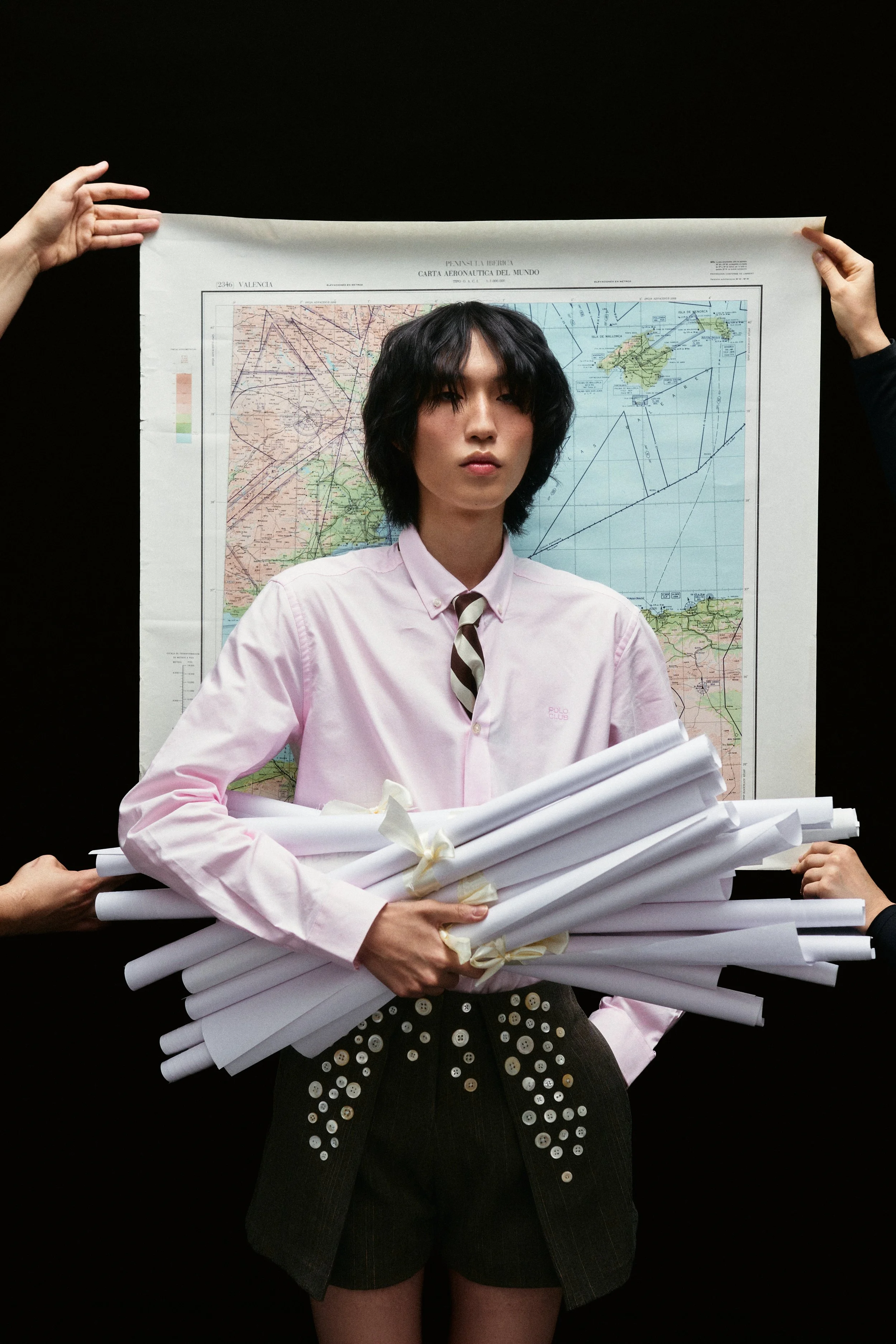 Person holding a rolled-up scroll in front of a map, with hands supporting it from both sides, against a black background.