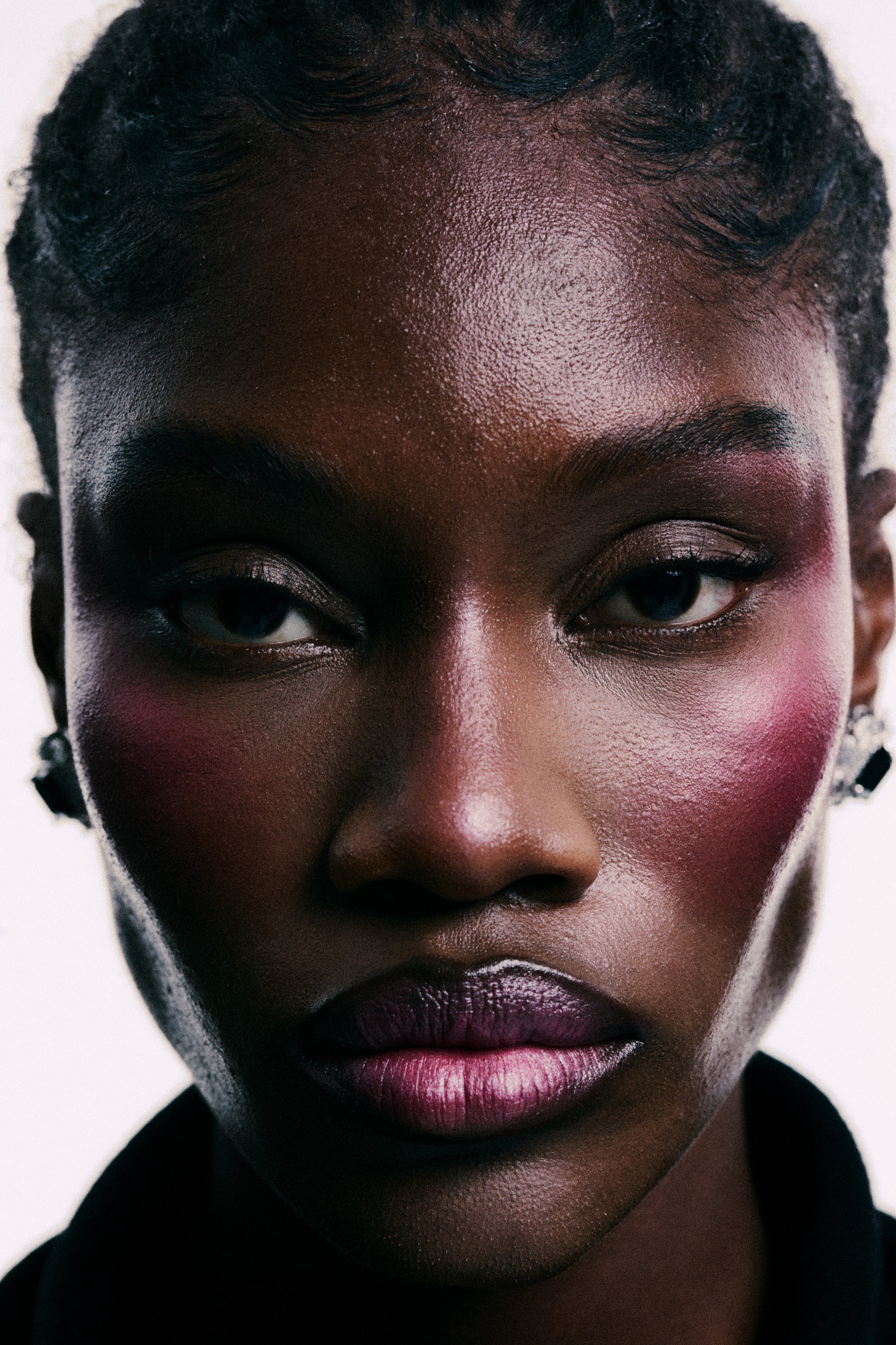 Close-up of a woman's face showing her forehead, eyes, nose, and lips with makeup, against a plain background.