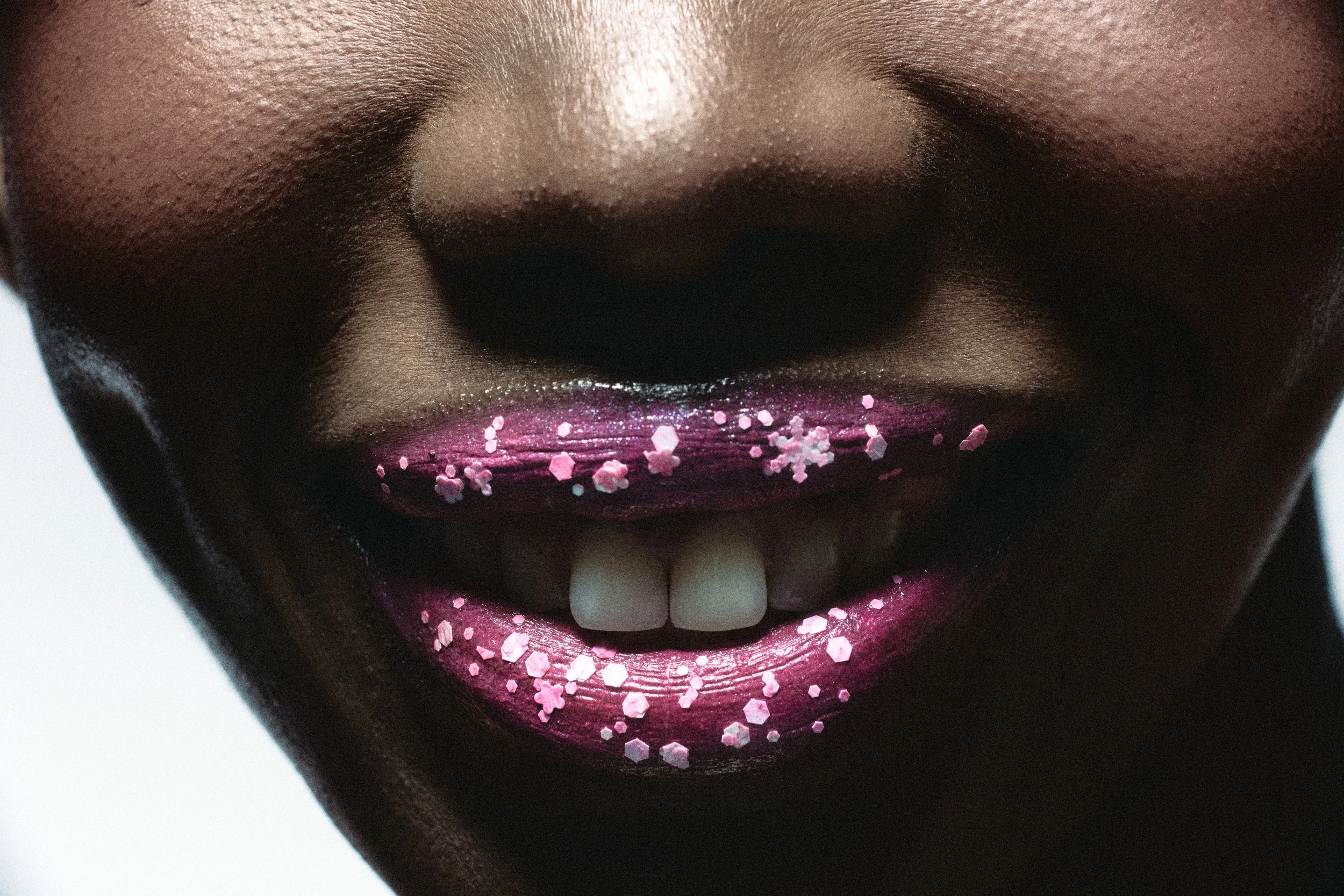 Close-up of a person's mouth with dark lipstick and pink heart-shaped and hexagonal glitter on the lips.