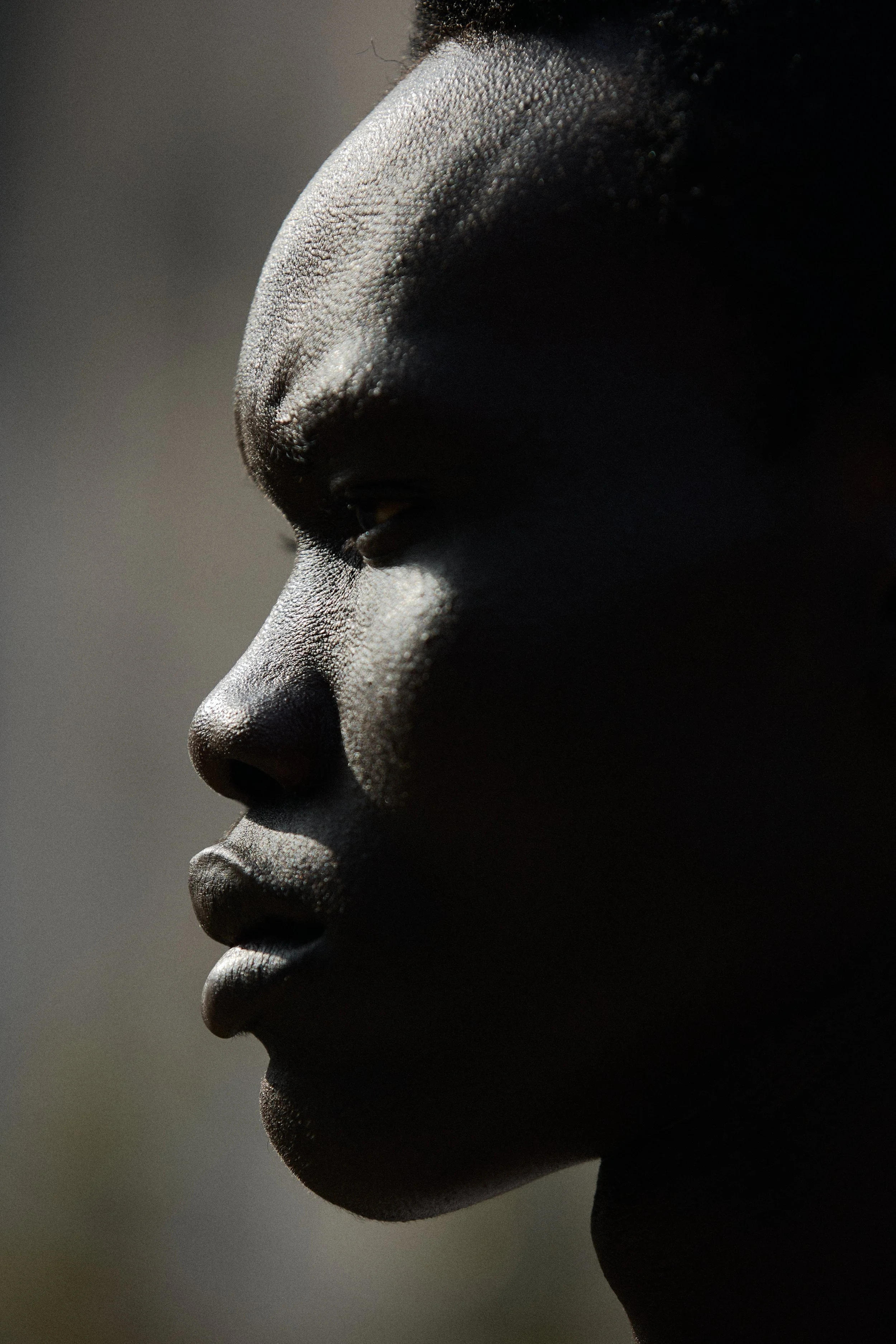Close-up side profile of a dark-skinned person's face, showing features from the forehead to the chin, with a shadowed background.