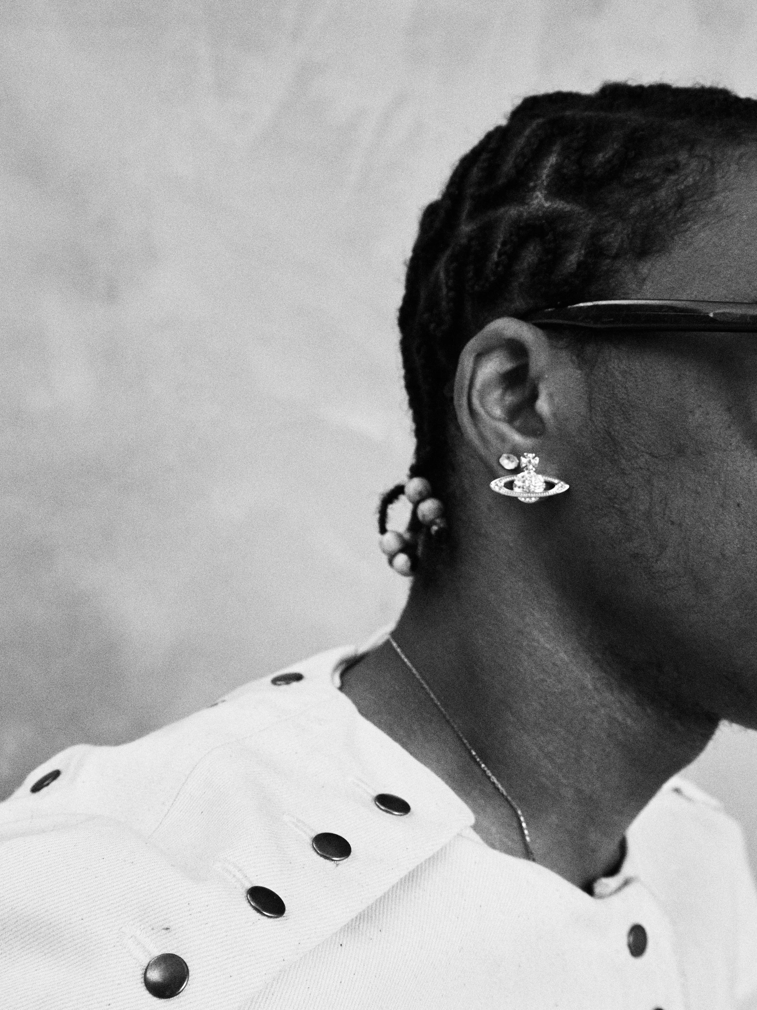 A close-up black and white photo of an African American woman wearing a polka dot shirt, a large earring, and glasses. She has braided hair with beads.
