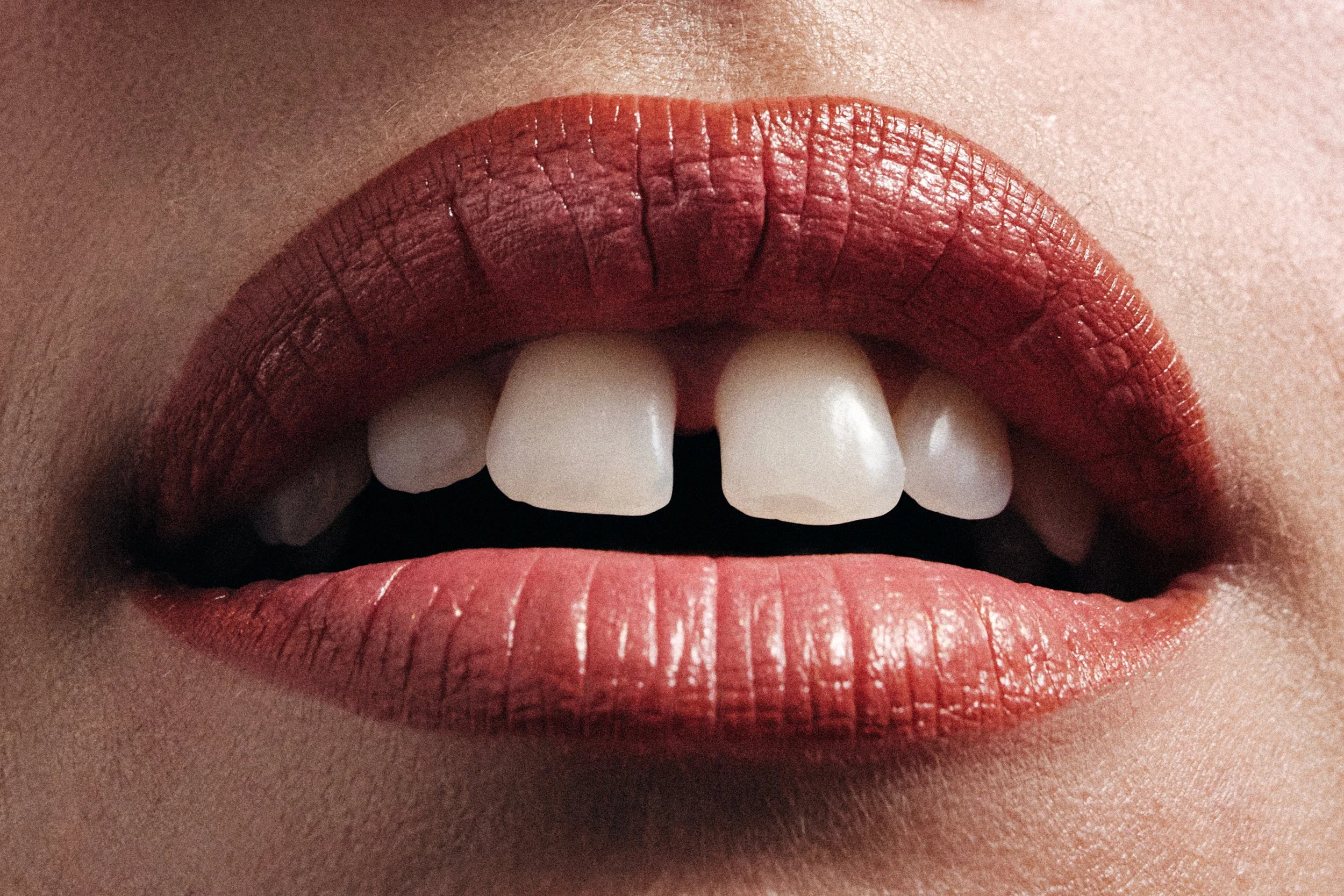Close-up of lips with red lipstick, slightly parted revealing teeth.