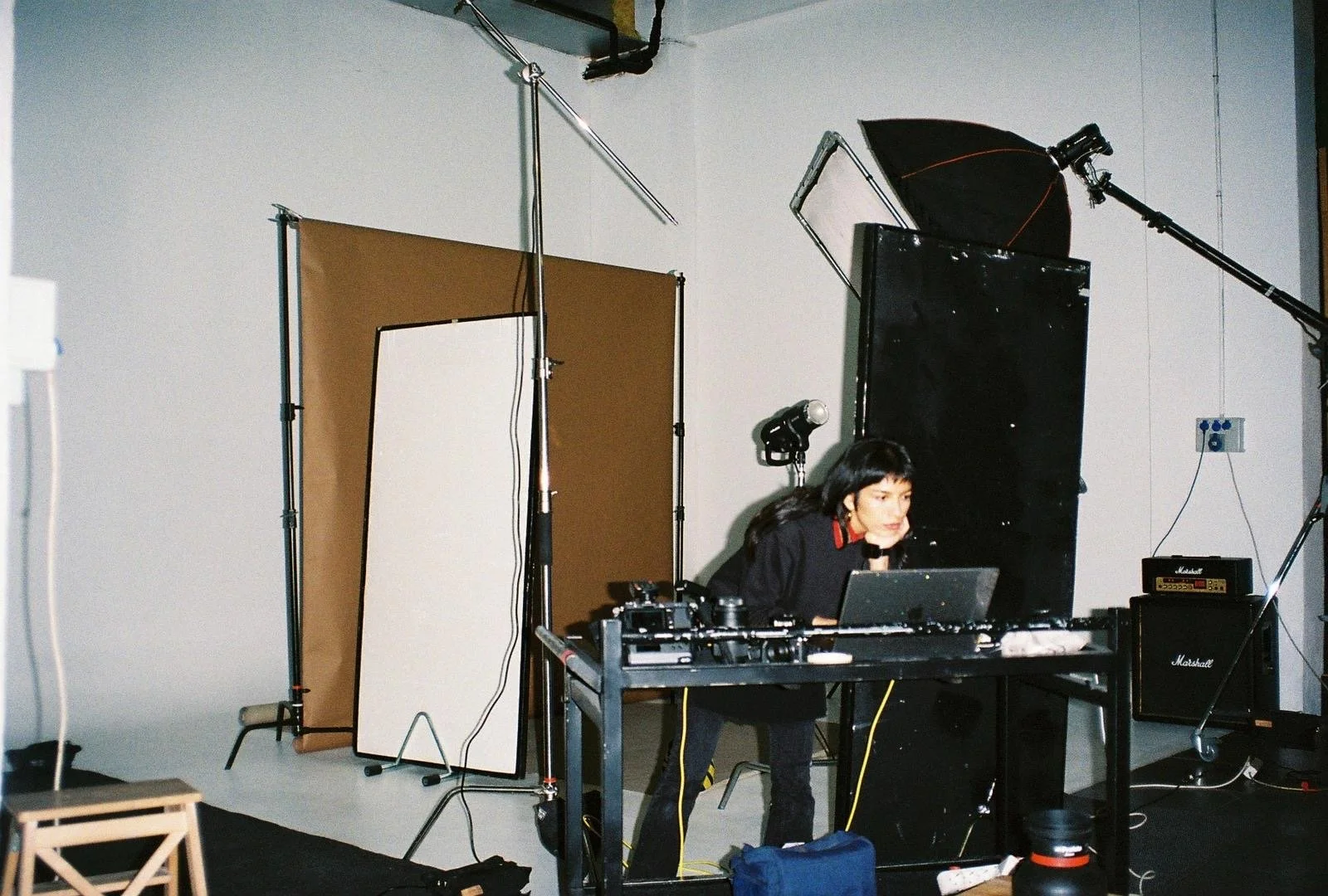 A woman operating photography or video equipment in a studio setting with lighting and backdrops around her.