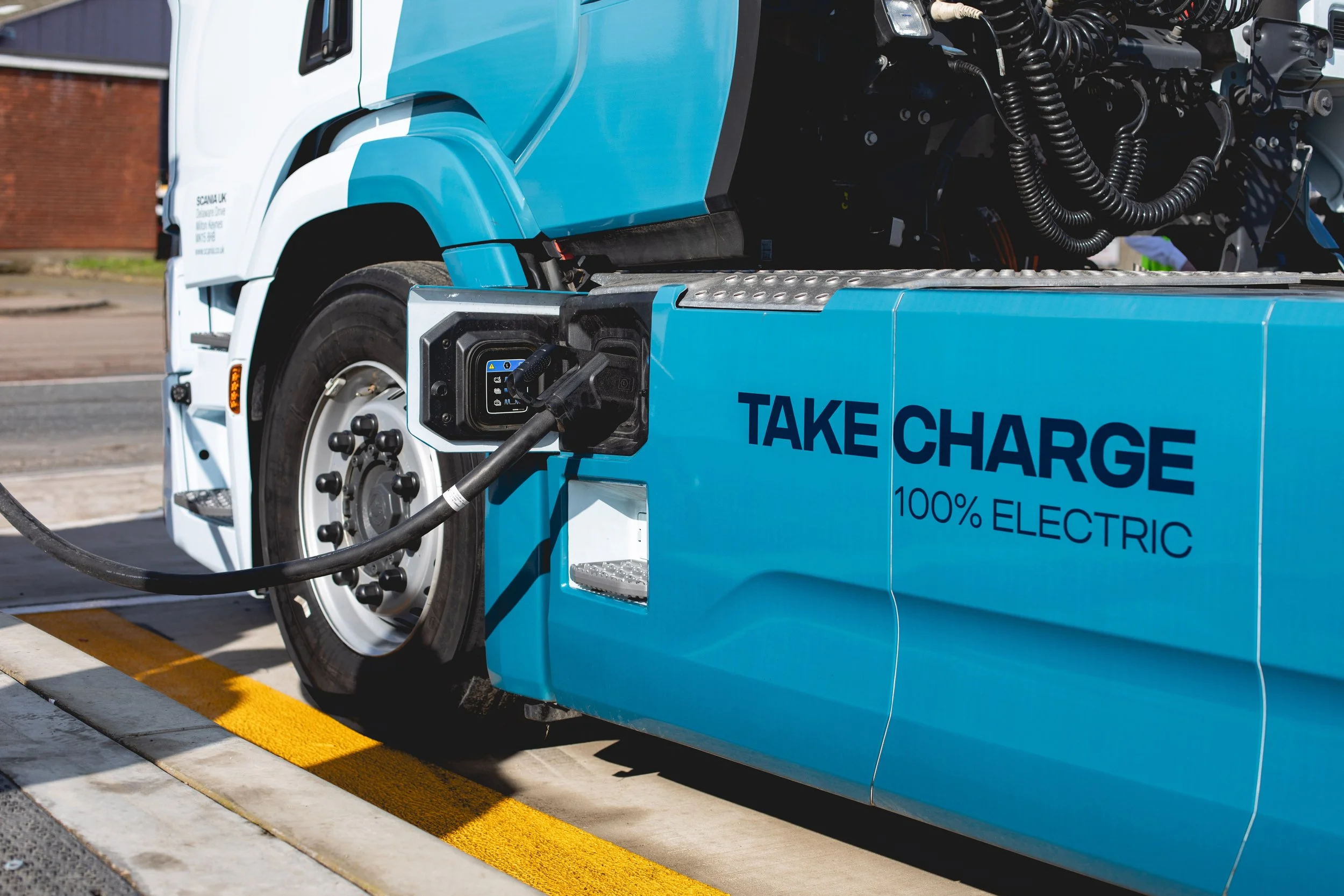 Blue electric taxi cab charging at a charging station with a yellow curb marking.