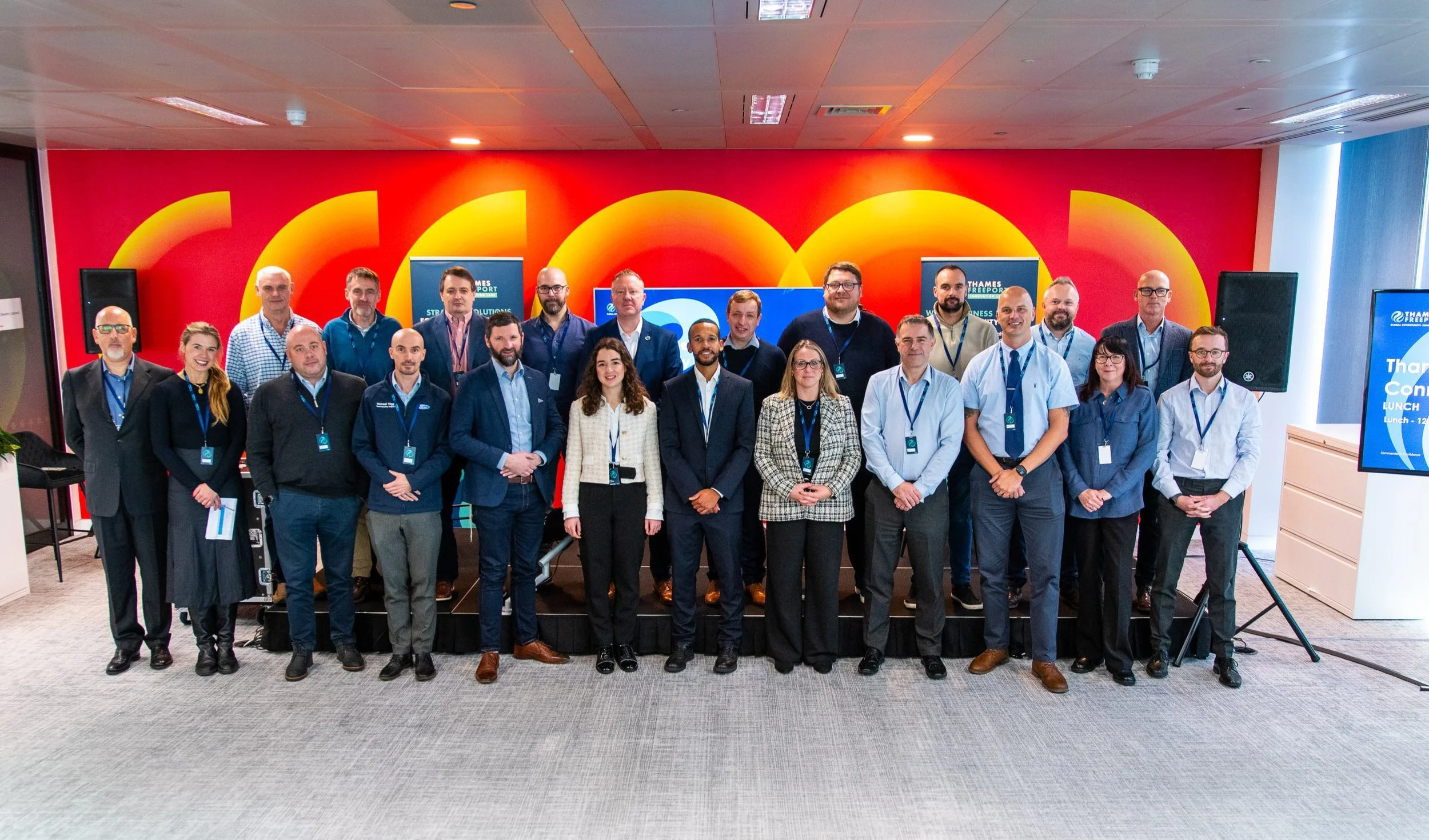 Group of professionals posing for a photo at a conference in front of a colorful abstract wall with London-based Thames Freeport banners displayed.
