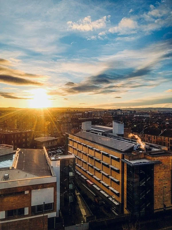 Cityscape at sunset with modern buildings and a partly cloudy sky.