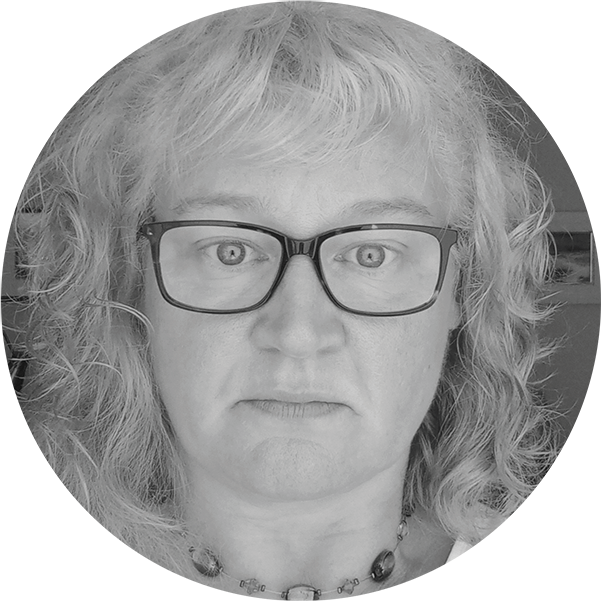 Black and white close-up photo of a woman with curly hair, wearing glasses, looking directly at the camera.