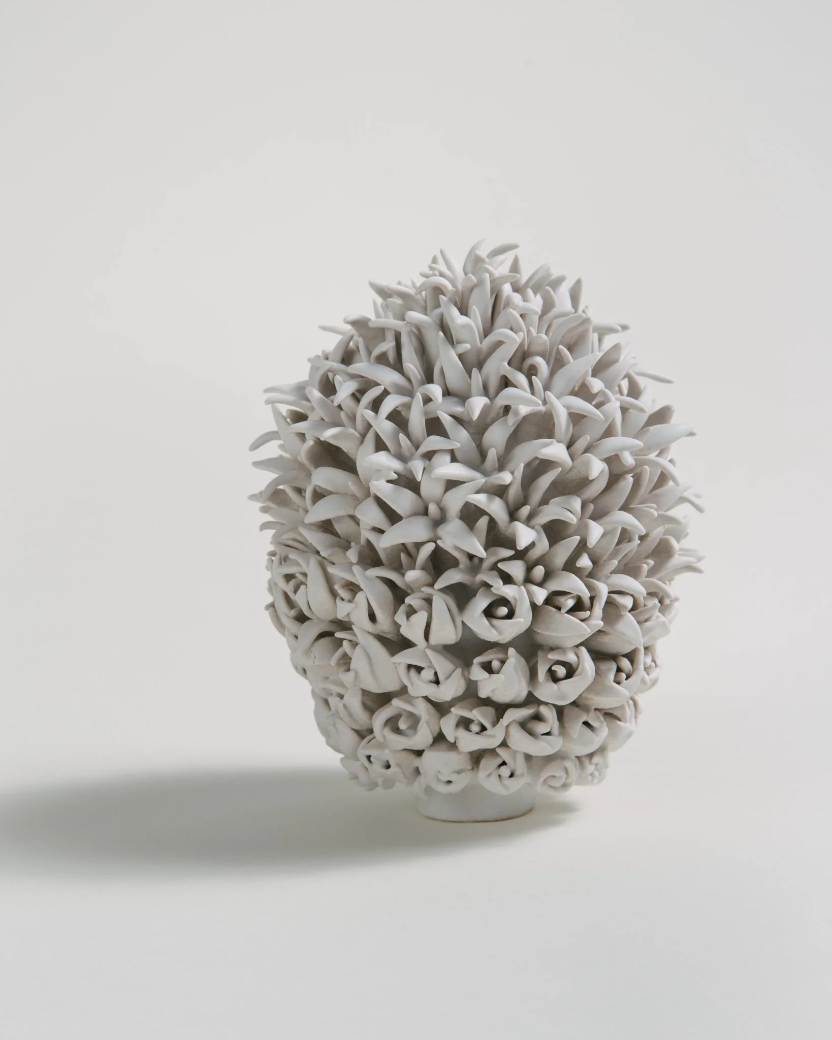 White ceramic vase with intricate carved floral pattern, placed on a reflective surface against a plain background.