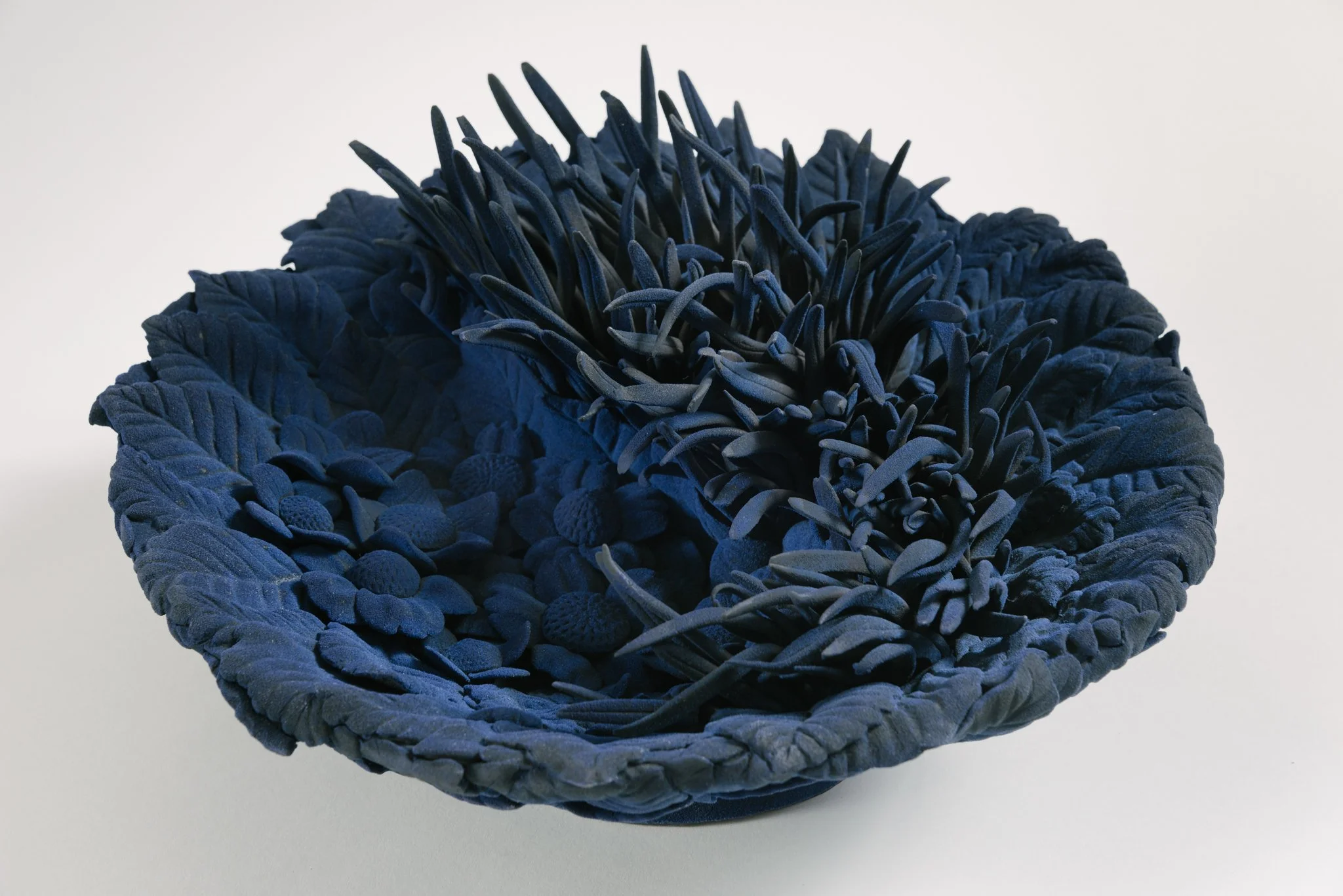 A navy blue textured decorative bowl with intricate woven design, set against a plain light background.