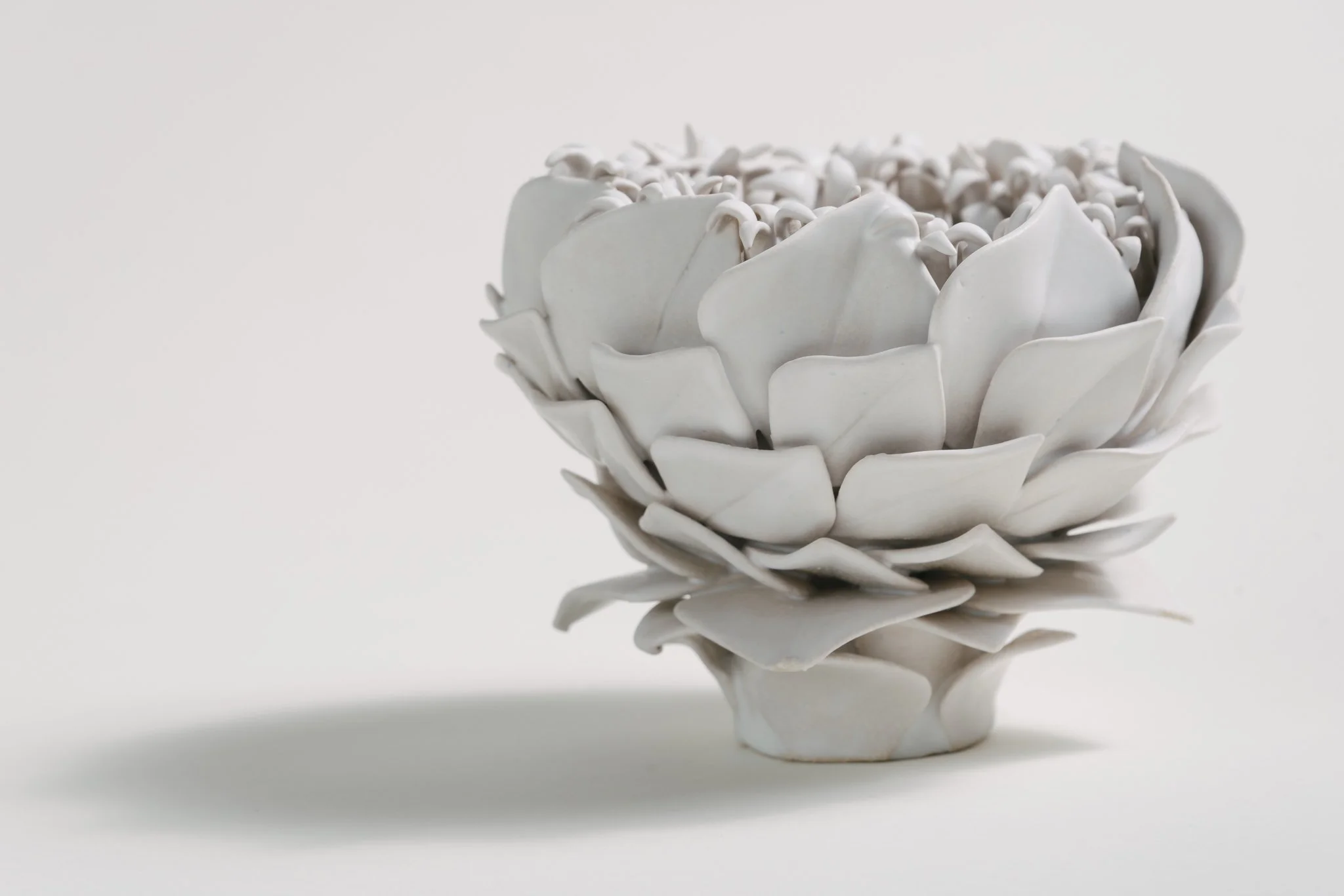 A white ceramic bowl resembling a flower with petals, filled with small white objects, on a white background.