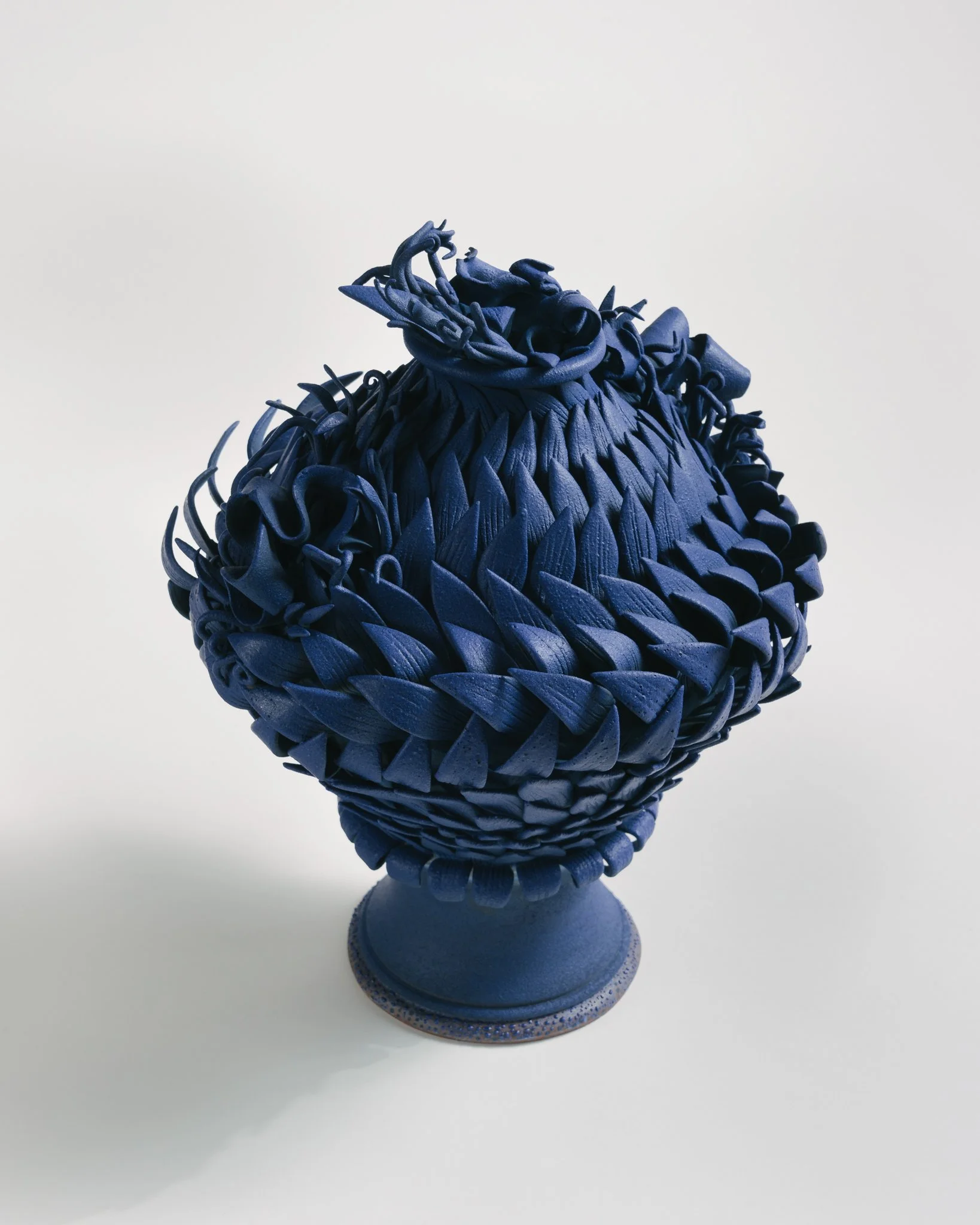 A blue artistic sculpture of a bird on a stand, made from layered and sculpted materials, with a smooth and glossy finish.