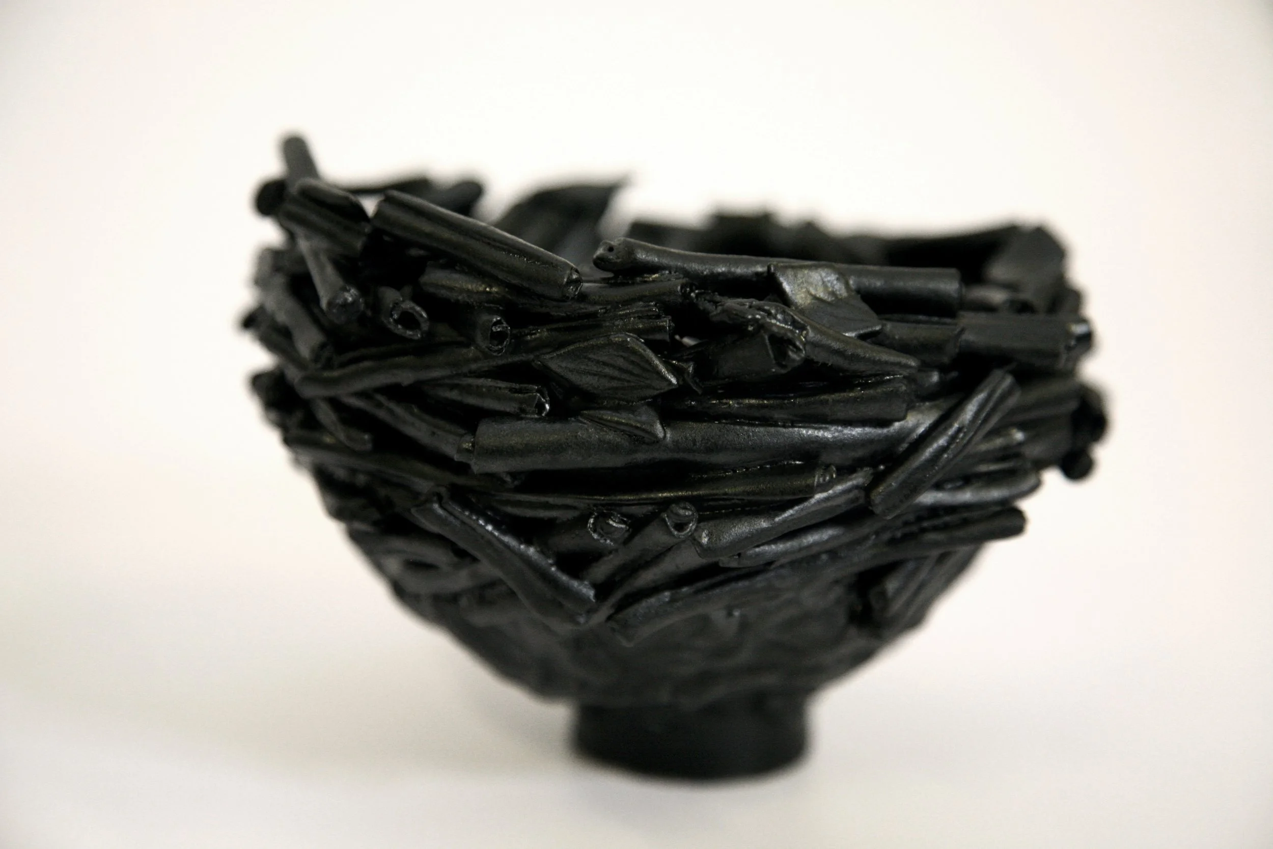 A small black bowl made of intertwined twigs or sticks containing black licorice candies on a white surface.