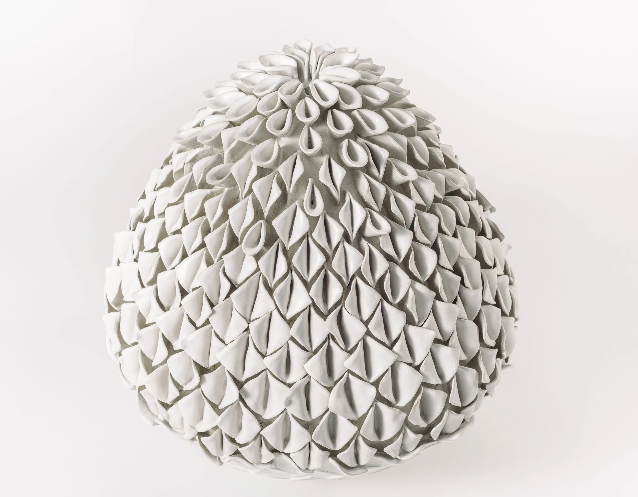 A close-up of a white ceramic sculpture with a textured, petal-like surface arranged in a cone shape.